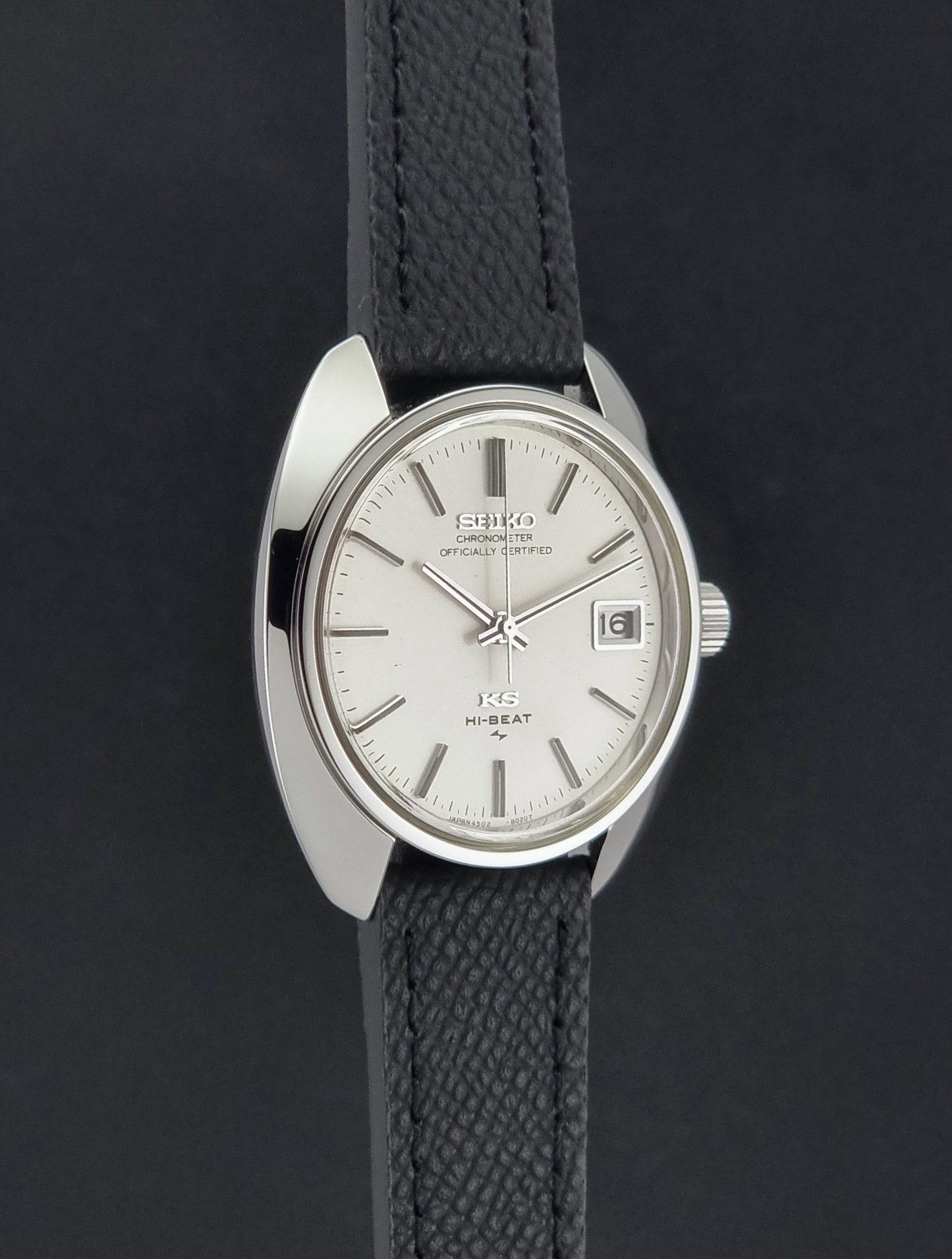 Vintage King Seiko Wristwatch 4502-8010 with a silver-toned metal case, white dial, and black textured leather strap, on a dark background side profile view