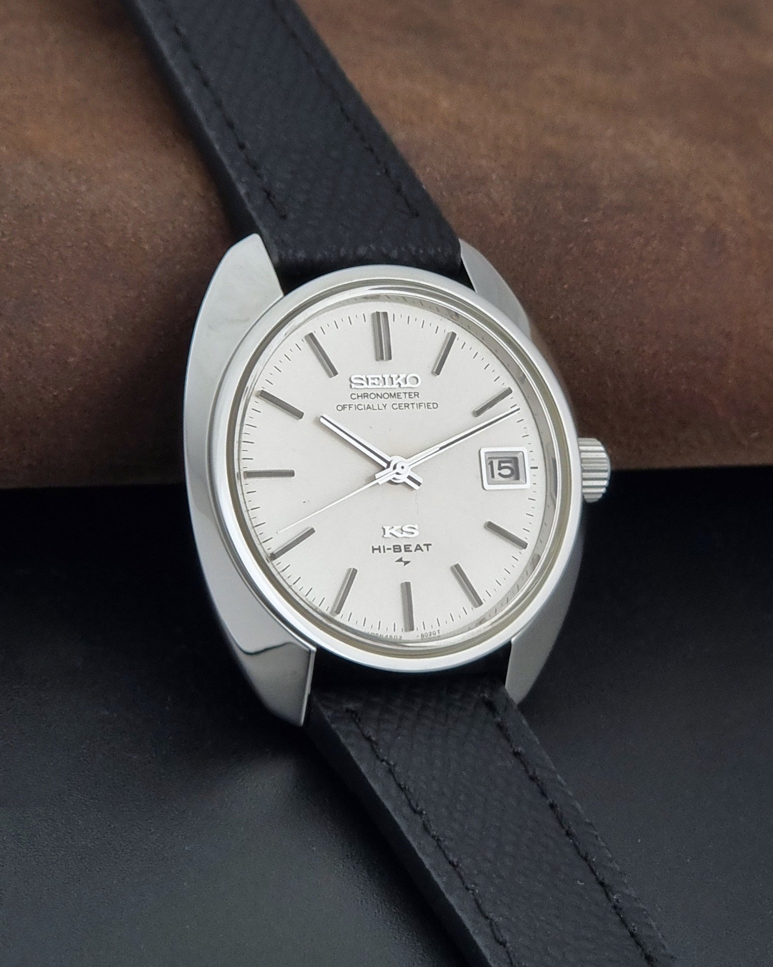 Vintage King Seiko Wristwatch 4502-8010 with a silver-toned metal case, white dial, and black textured leather strap, on a dark background side view