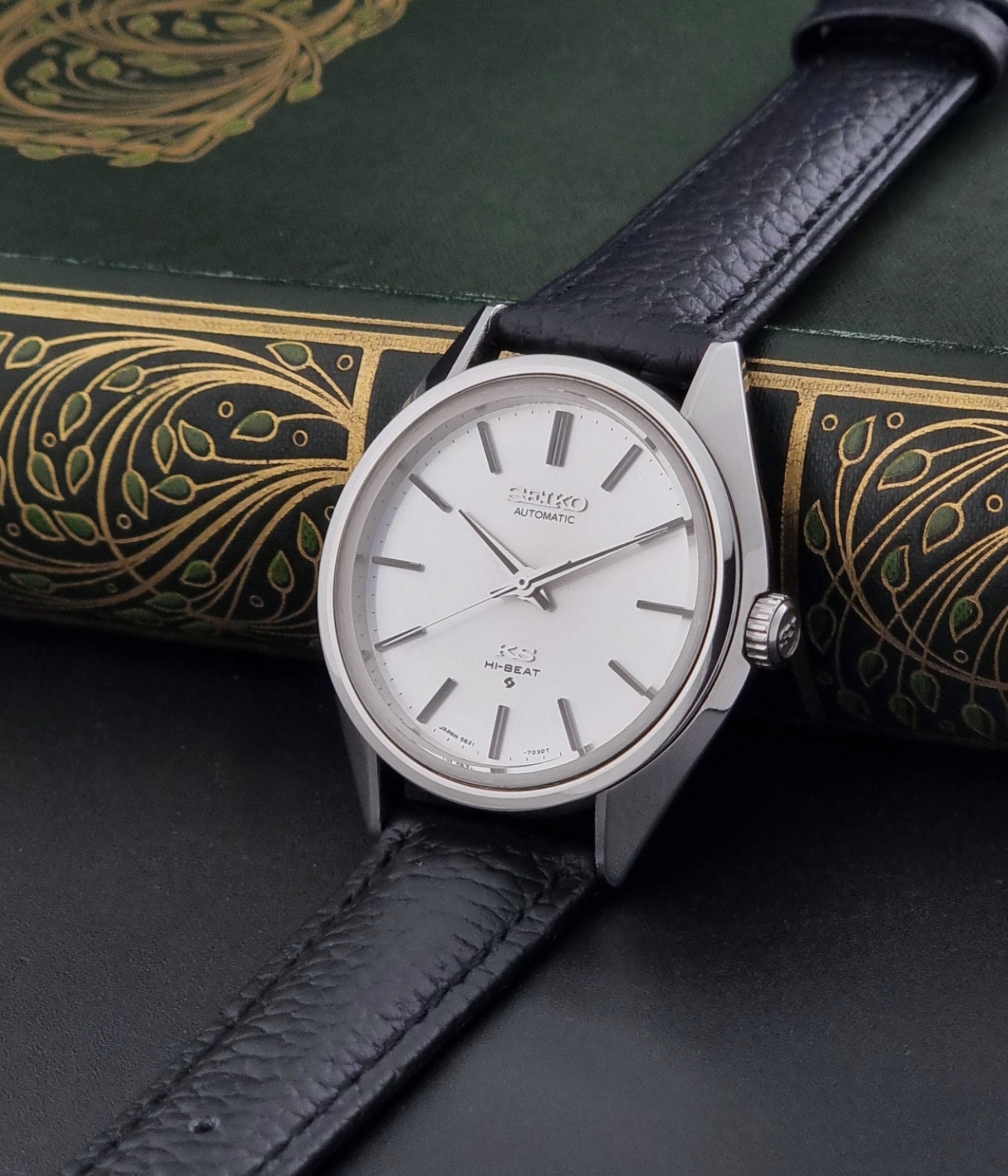 Vintage King Seiko Wristwatch 5621-7022 with a dark leather strap on a green background crown view