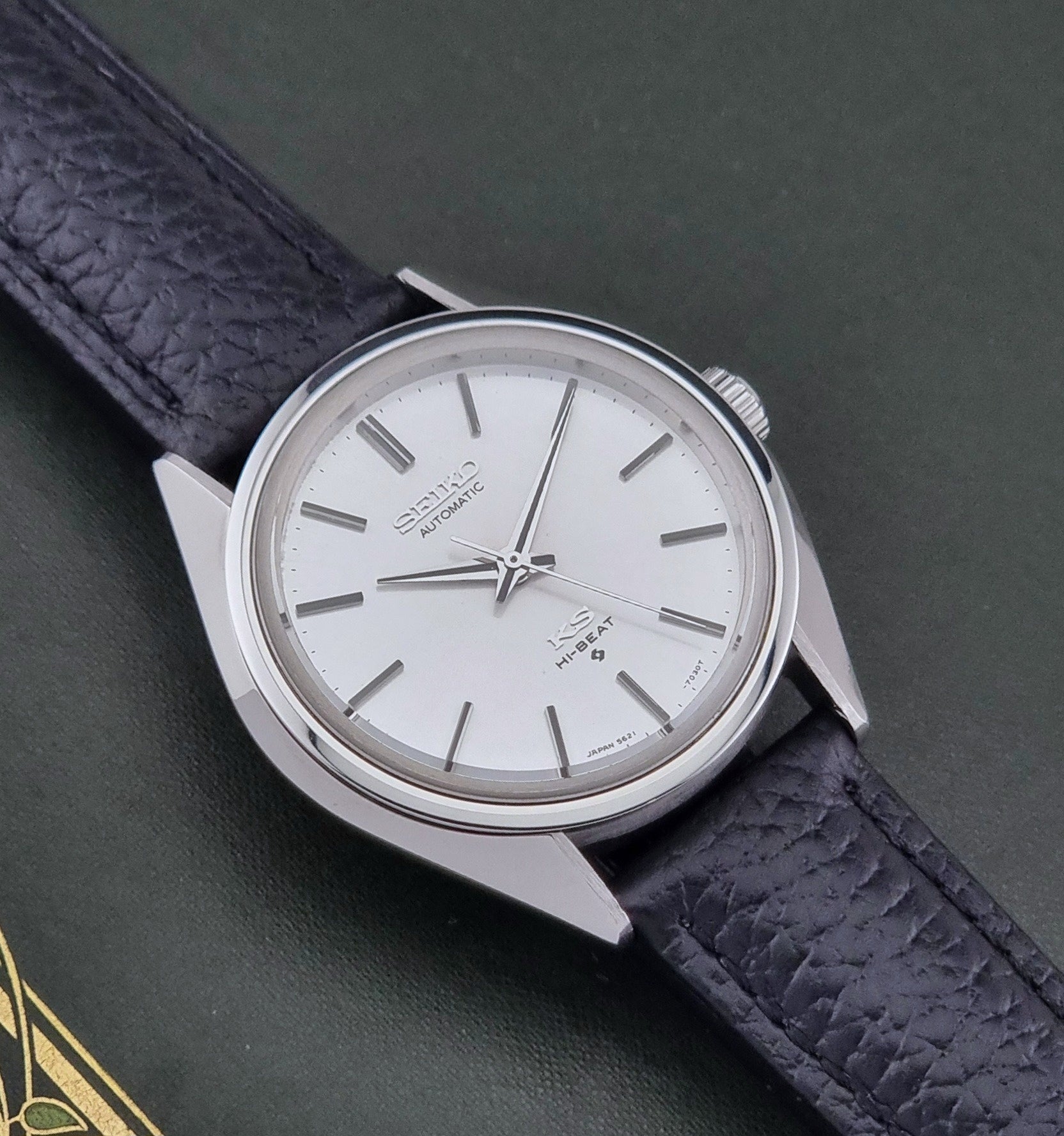 Vintage King Seiko Wristwatch 5621-7022 with a dark leather strap on a green background close up dial view