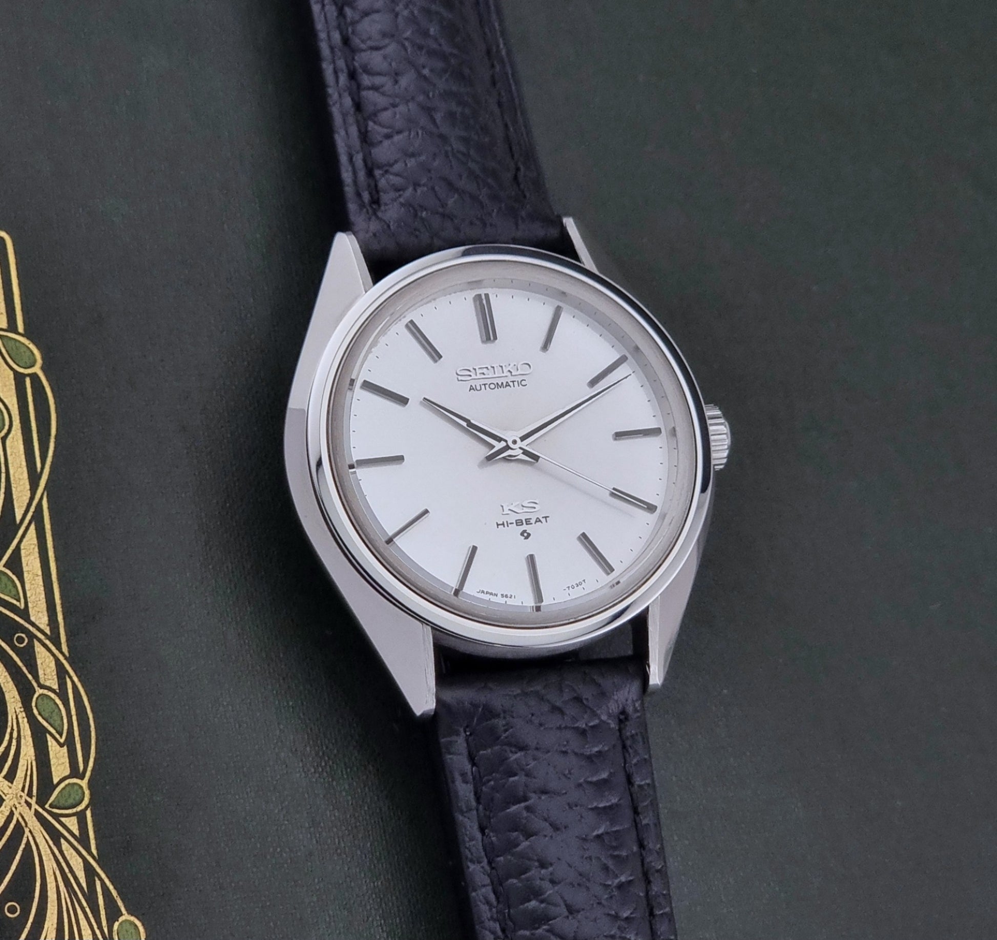 Vintage King Seiko Wristwatch 5621-7022 with a dark leather strap on a green background front view
