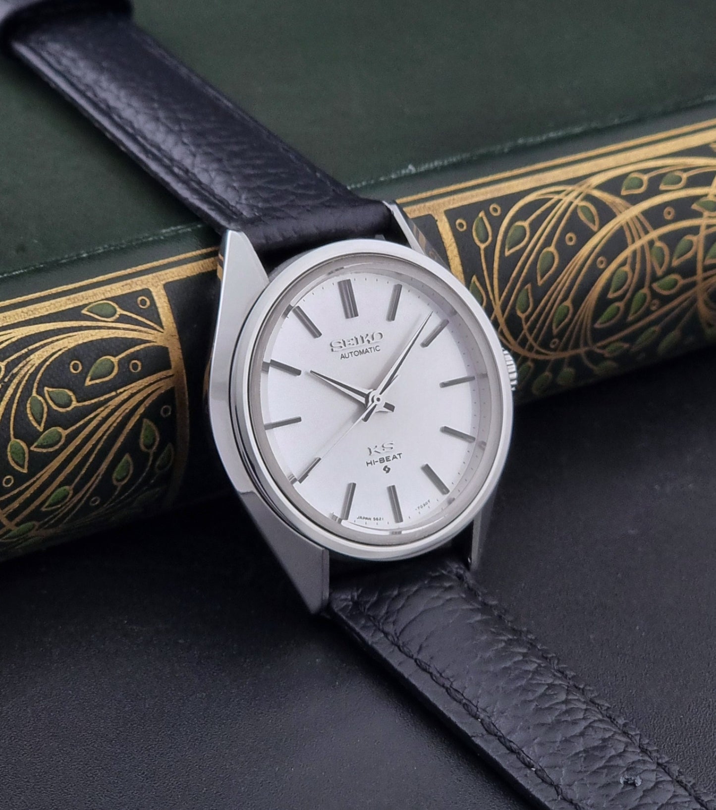 Vintage King Seiko Wristwatch 5621-7022 with a dark leather strap on a green background side view