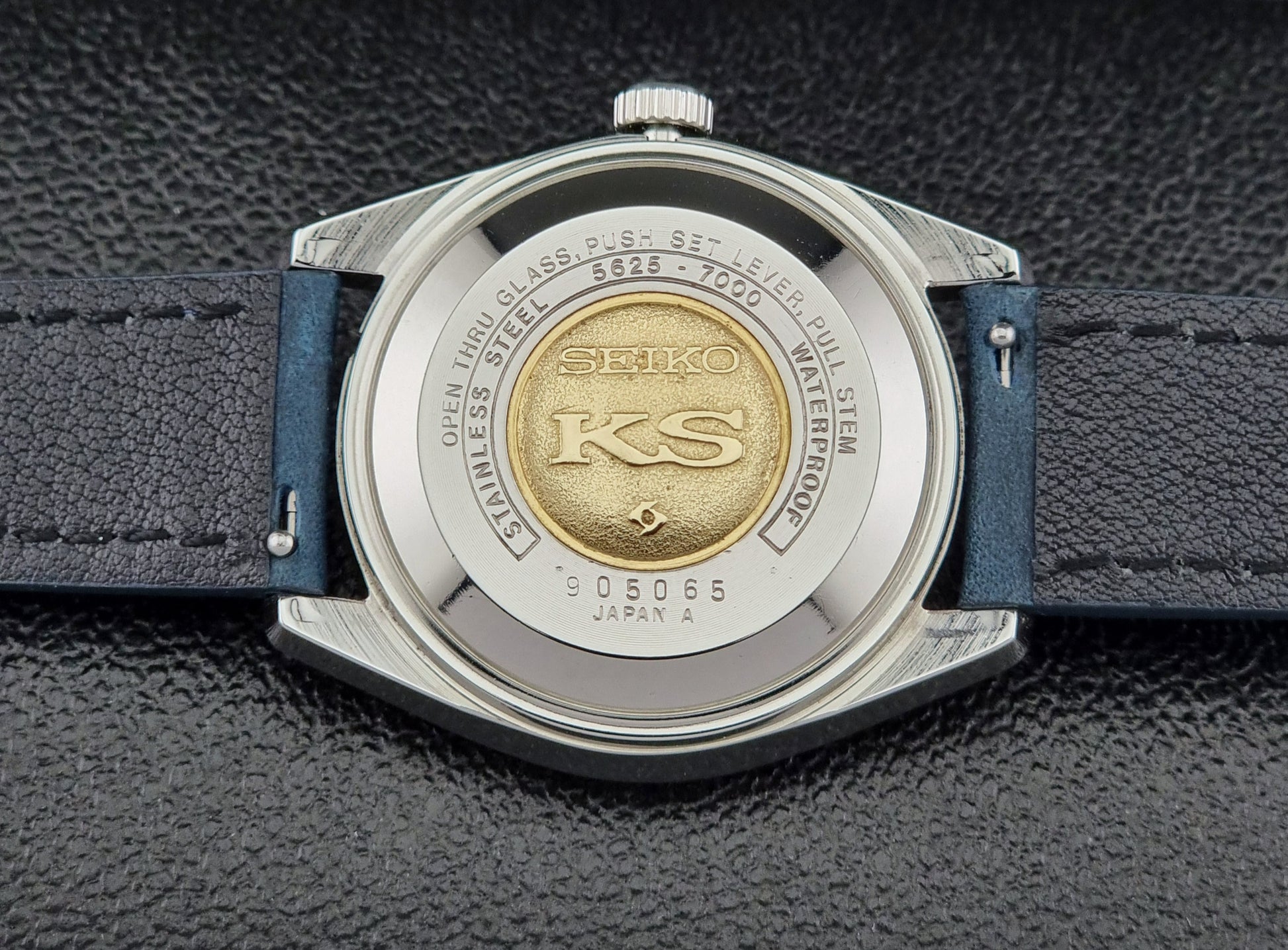 Vintage King Seiko 5625-7000 Wristwatch case back with blue strap and silver case on a dark textured background
