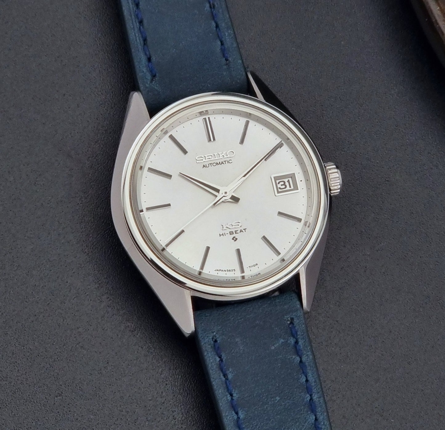 Vintage King Seiko Wristwatch 5625-7110 blue strap and silver case on a dark surface front view