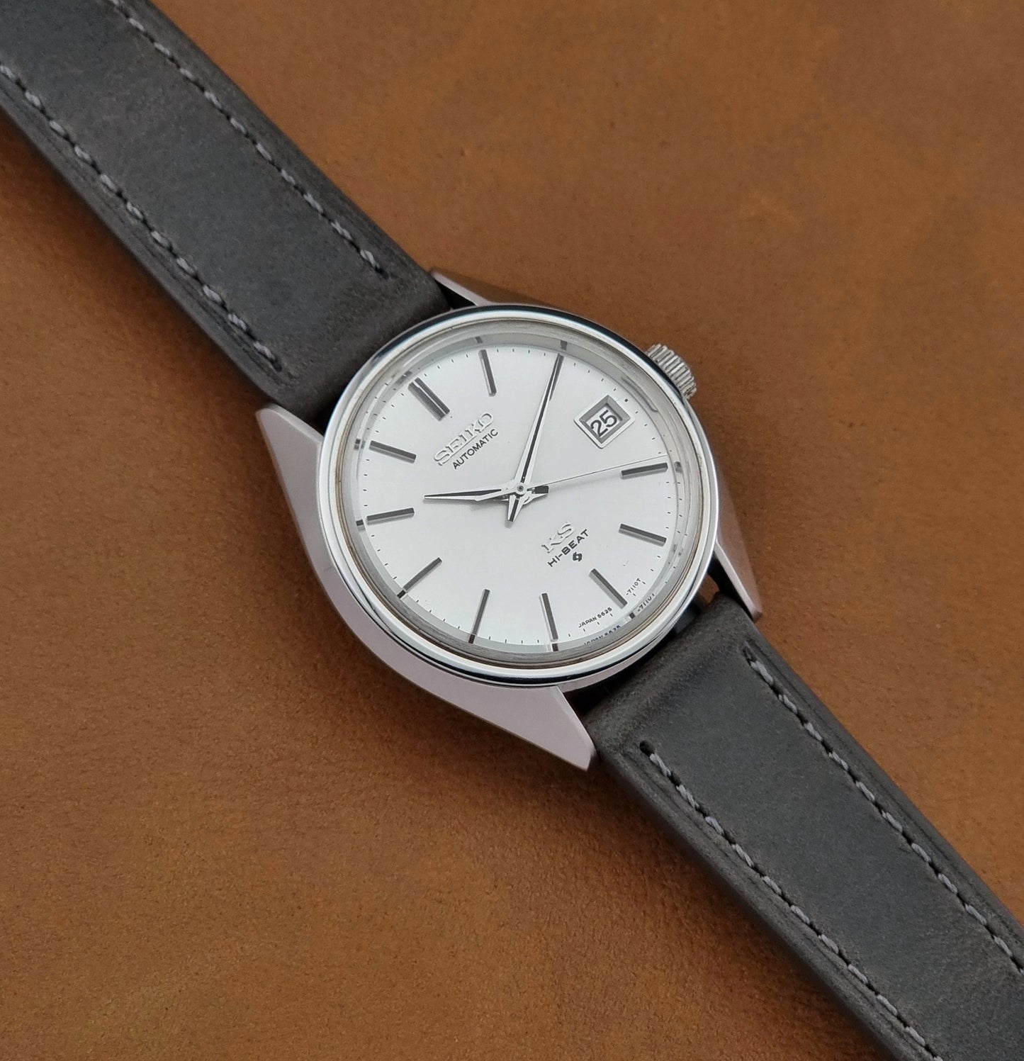 Vintage King Seiko 5625-7110 Wristwatch with a gray strap and white dial on a brown background close up dial view