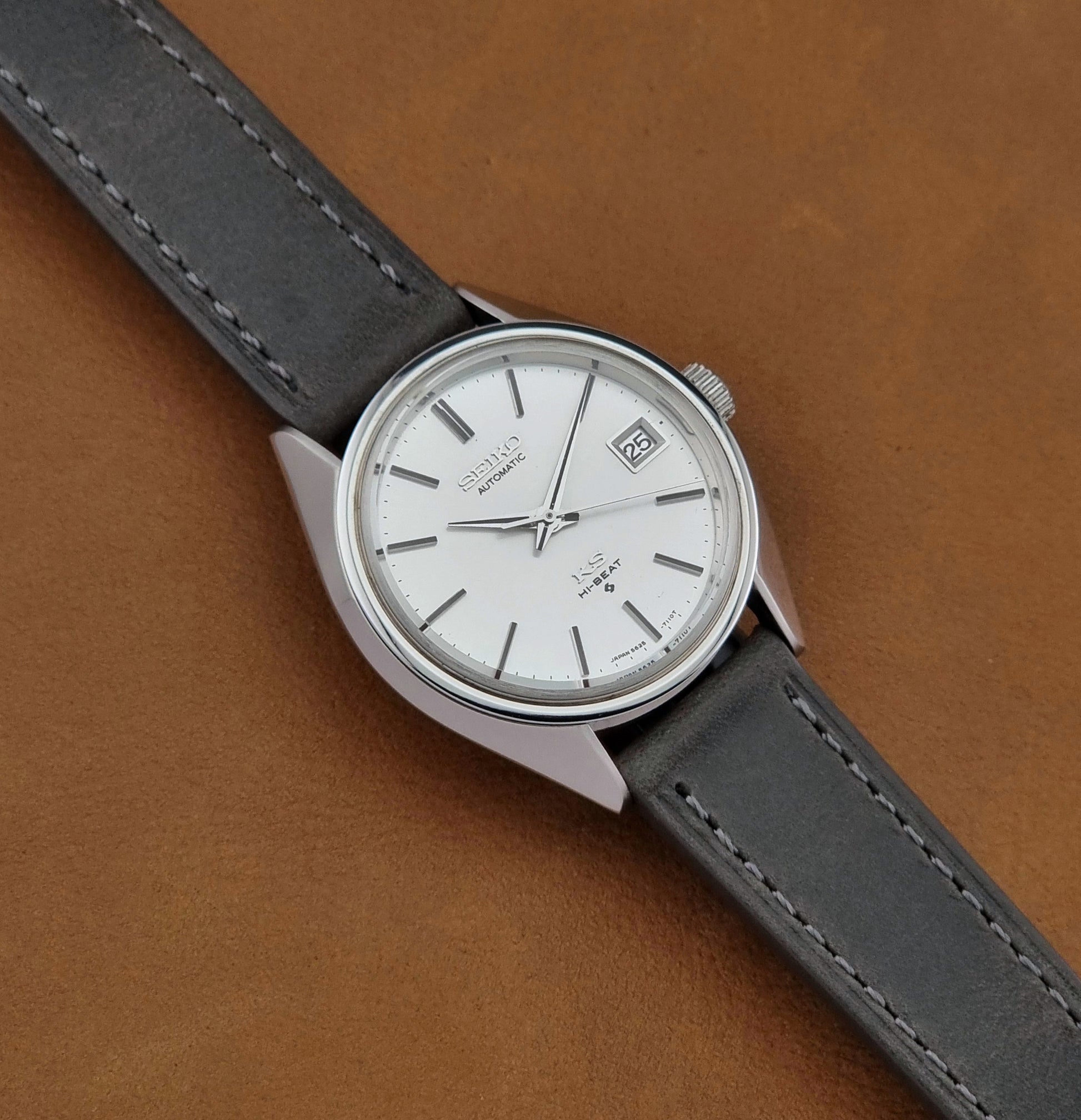 Vintage King Seiko 5625-7110 Wristwatch with a gray strap and white dial on a brown background close up dial view