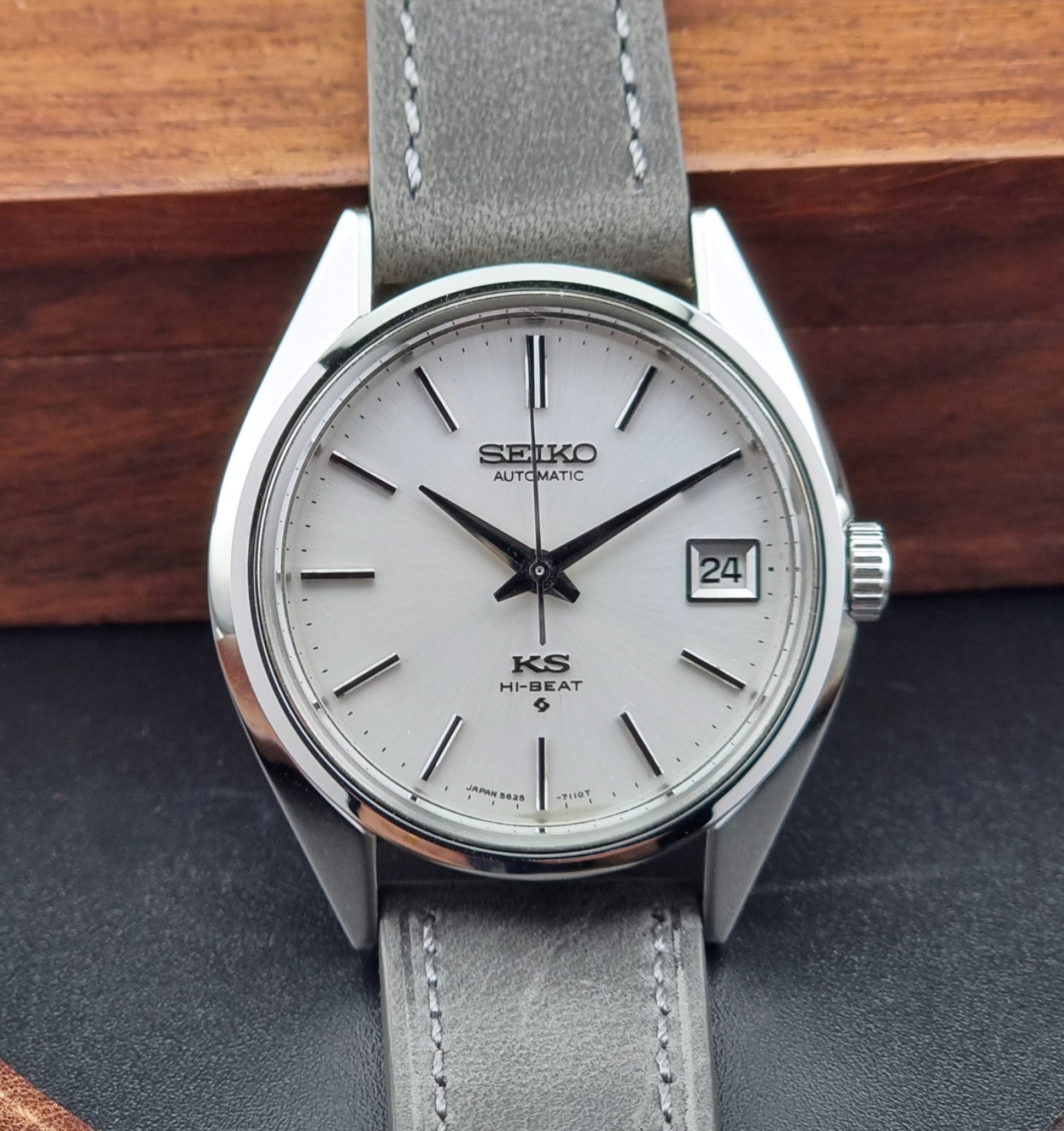 Vintage King Seiko watch with gray strap on a dark surface with wooden background