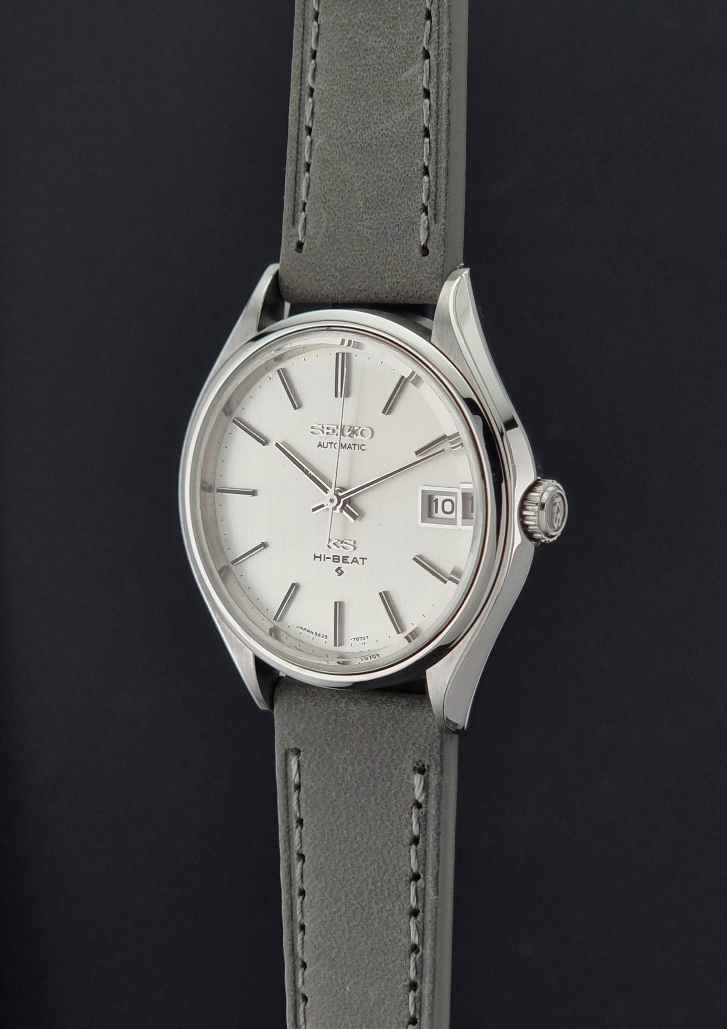 A Vintage King Seiko 5625-7121 watch with a silver-tone stainless steel case, white dial, and a gray leather strap, shown against a dark background.