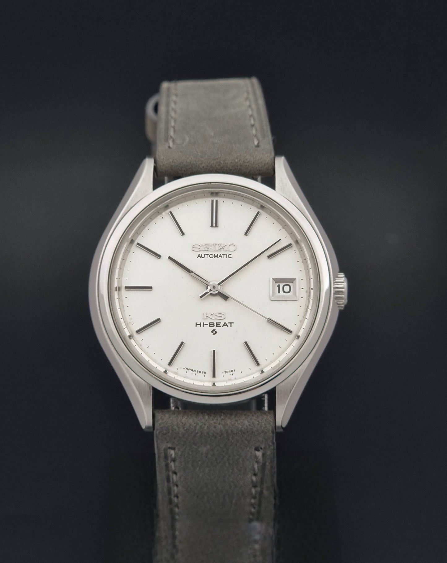 A Vintage King Seiko 5625-7121 watch with a silver stainless steel case, white dial, and a gray leather strap, shown against a dark background.