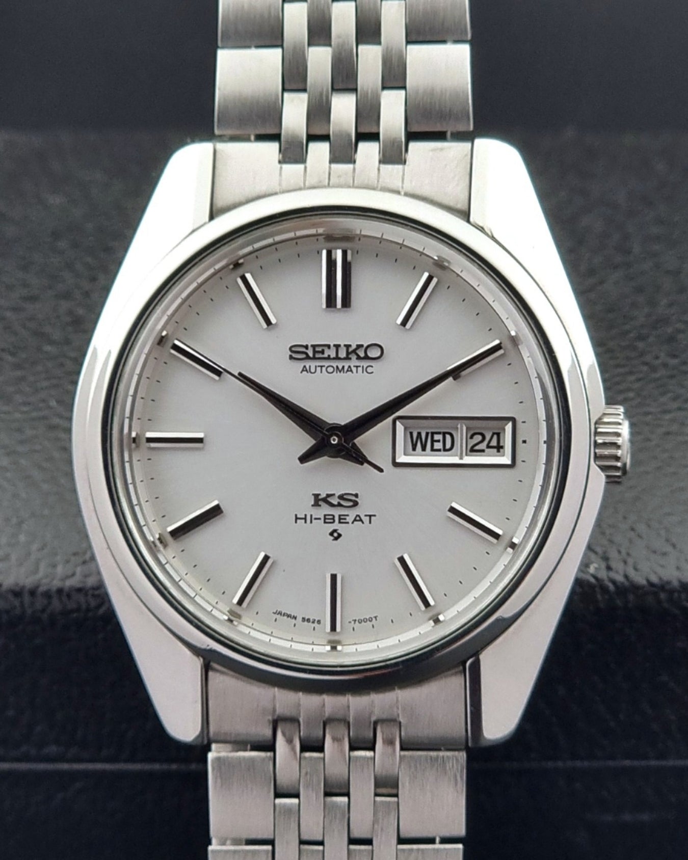 Silver Seiko watch with a metallic bracelet on a dark textured background