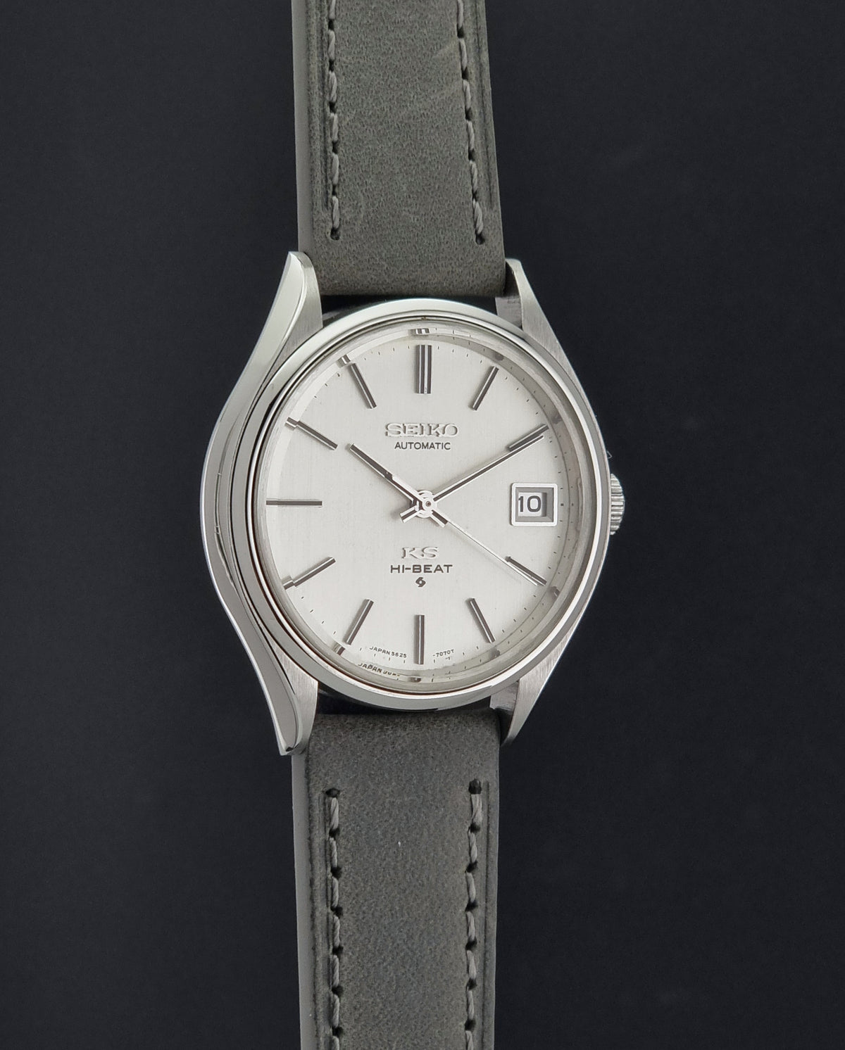 A Vintage King Seiko 5625-7121 watch with a silver-toned metal case, white dial, and a dark gray leather strap, shown against a dark background.