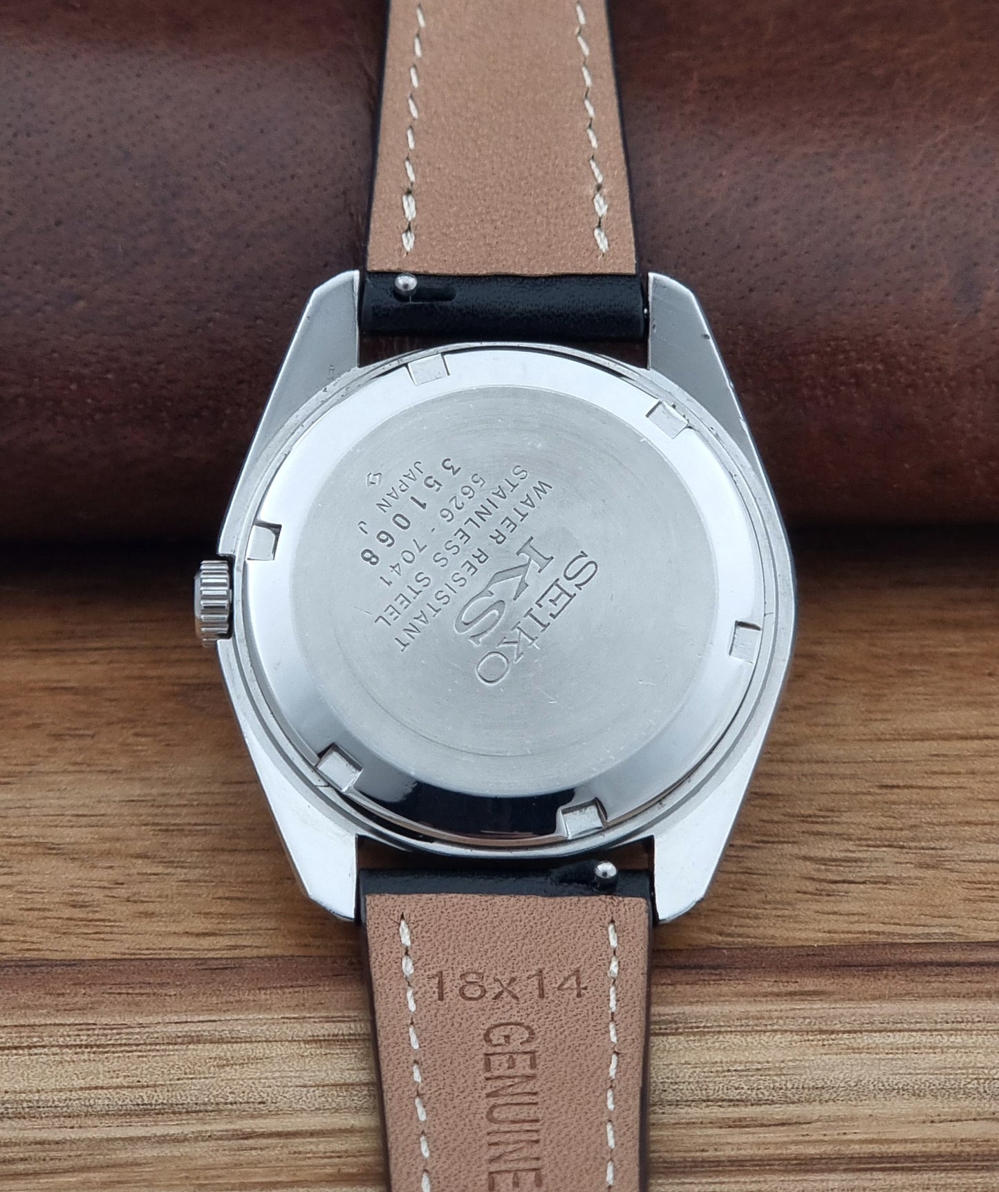 Vintage King Seiko watch 5626-7041  with a silver-toned metal case, white dial, and black leather strap with white stitching, on a wooden surface case back view