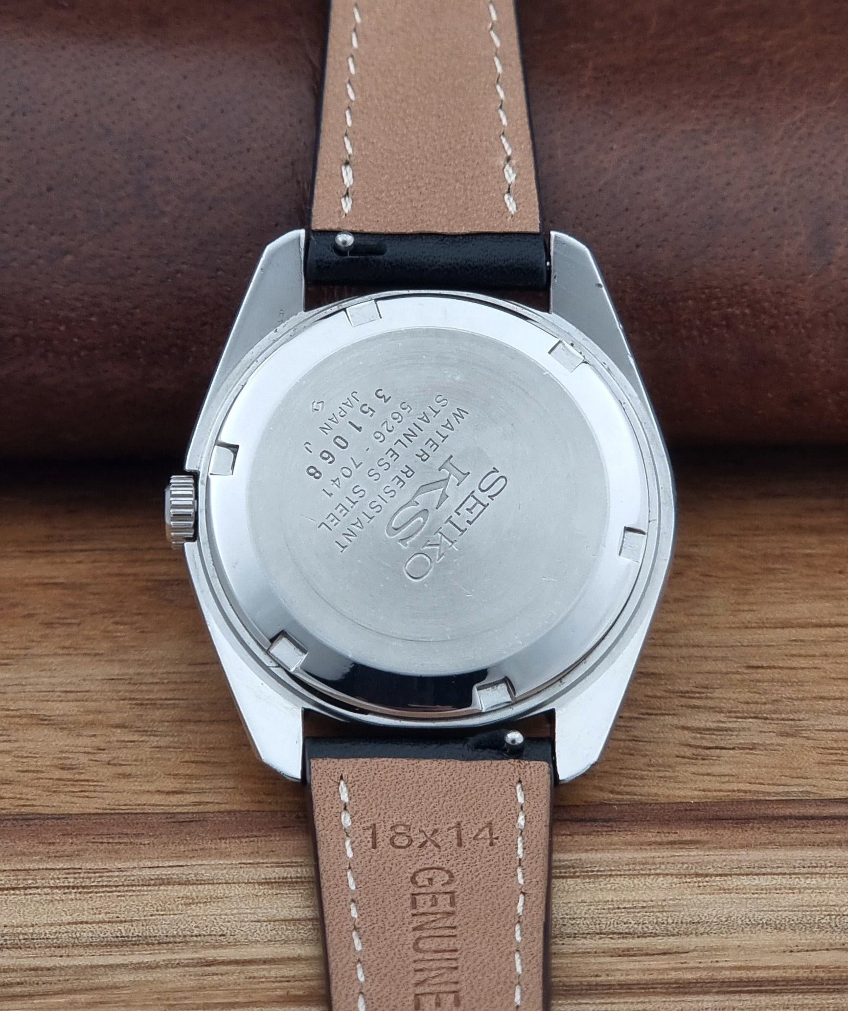 Vintage King Seiko watch 5626-7041  with a silver-toned metal case, white dial, and black leather strap with white stitching, on a wooden surface case back view
