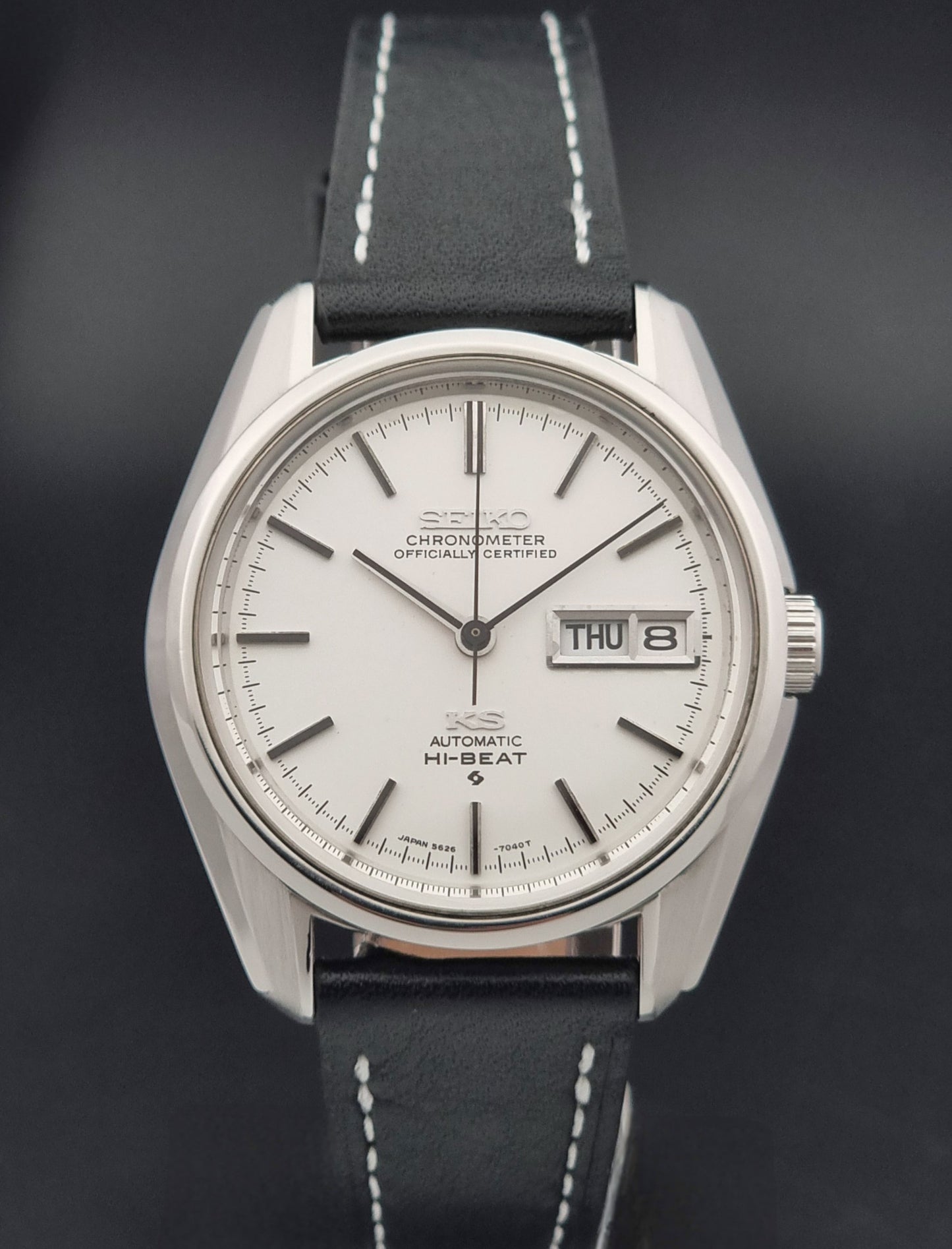 Vintage King Seiko watch 5626-7041  with a silver-toned metal case, white dial, and black leather strap with white stitching, on a wooden surface close dial view
