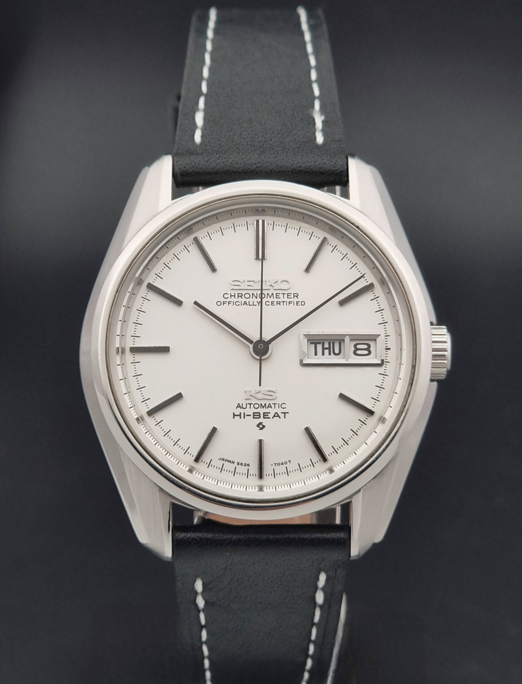 Vintage King Seiko watch 5626-7041  with a silver-toned metal case, white dial, and black leather strap with white stitching, on a wooden surface close dial view