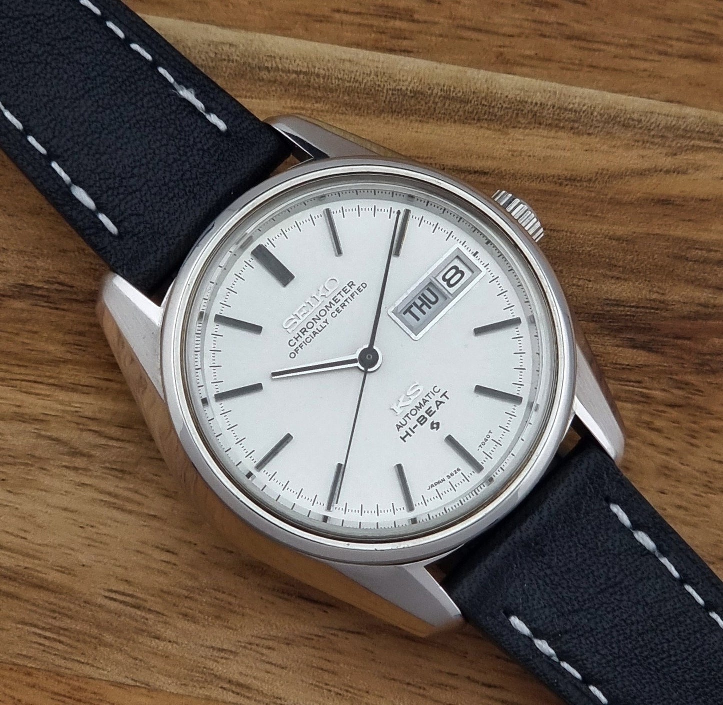 Vintage King Seiko watch 5626-7041  with a silver-toned metal case, white dial, and black leather strap with white stitching, on a wooden surface close up dial view