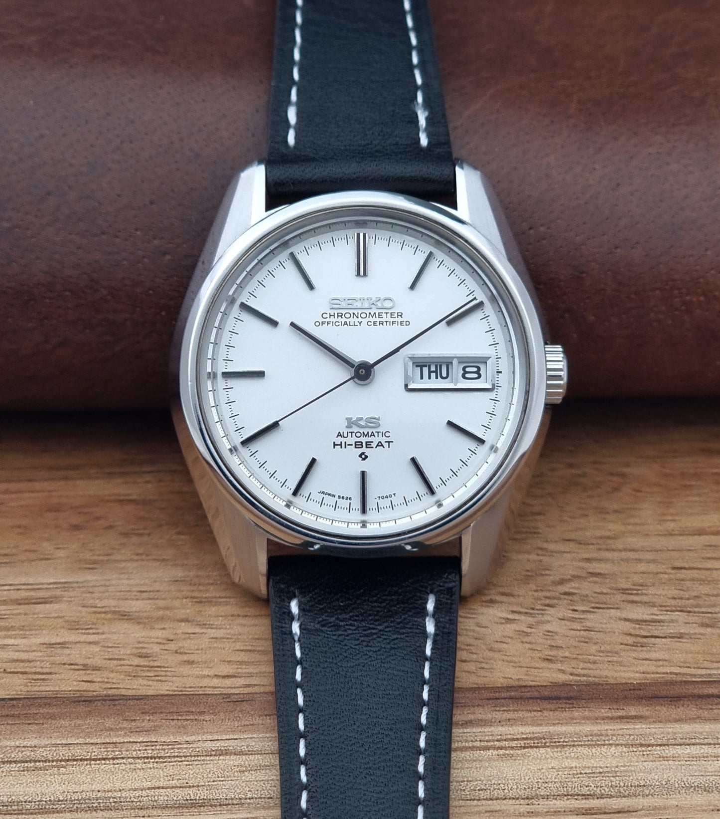 Vintage King Seiko watch 5626-7041  with a silver-toned metal case, white dial, and black leather strap with white stitching, on a wooden surface dial view