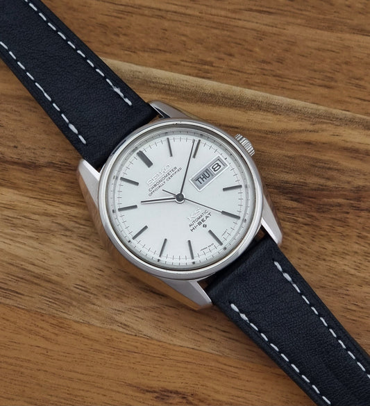 Vintage King Seiko watch 5626-7041  with a silver-toned metal case, white dial, and black leather strap with white stitching, on a wooden surface dial