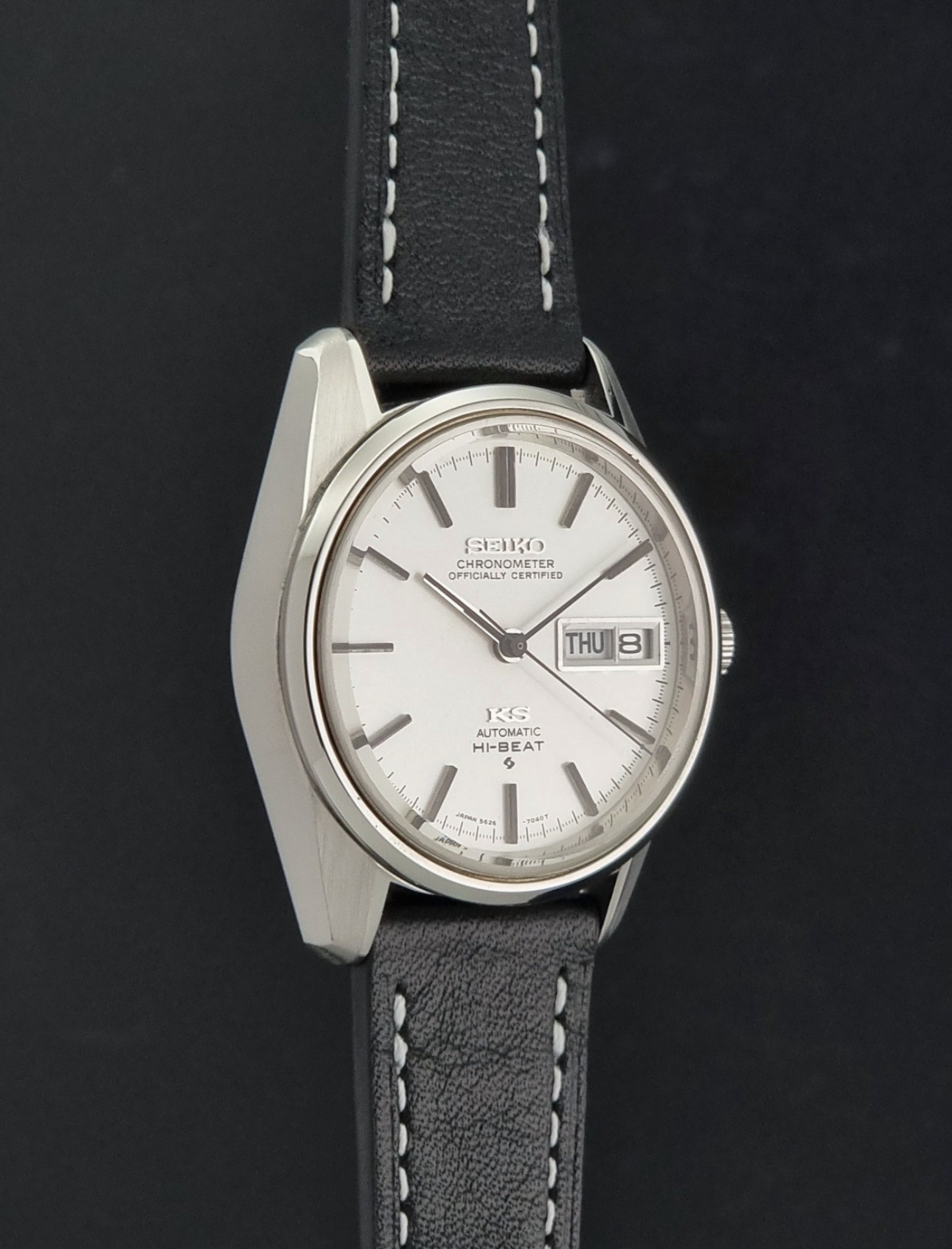 Vintage King Seiko watch 5626-7041  with a silver-toned metal case, white dial, and black leather strap with white stitching, on a dark background side profile view