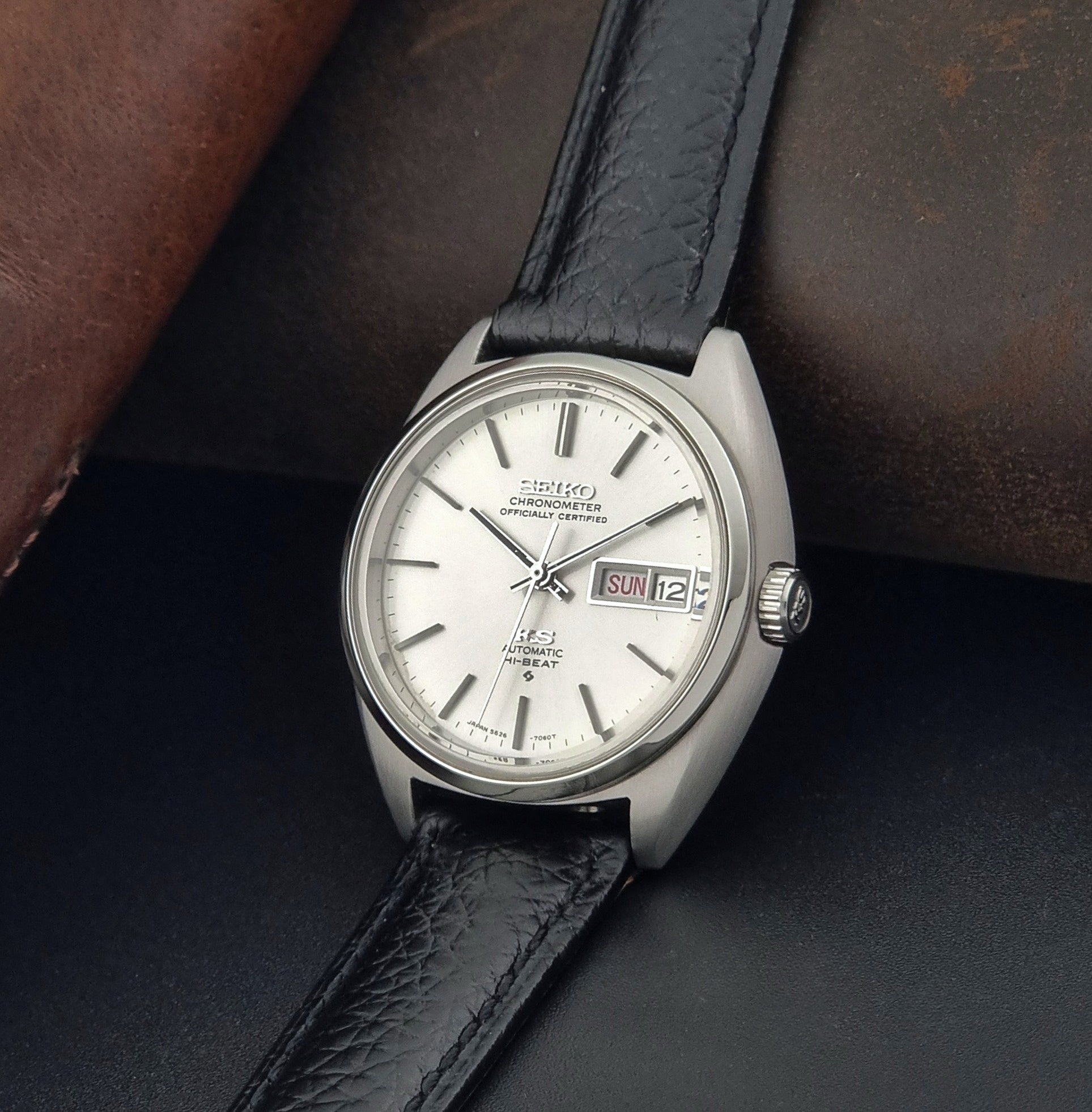 Vintage King Seiko 5626-7060 wristwatch with a silver case and black leather strap on a dark surface crown view