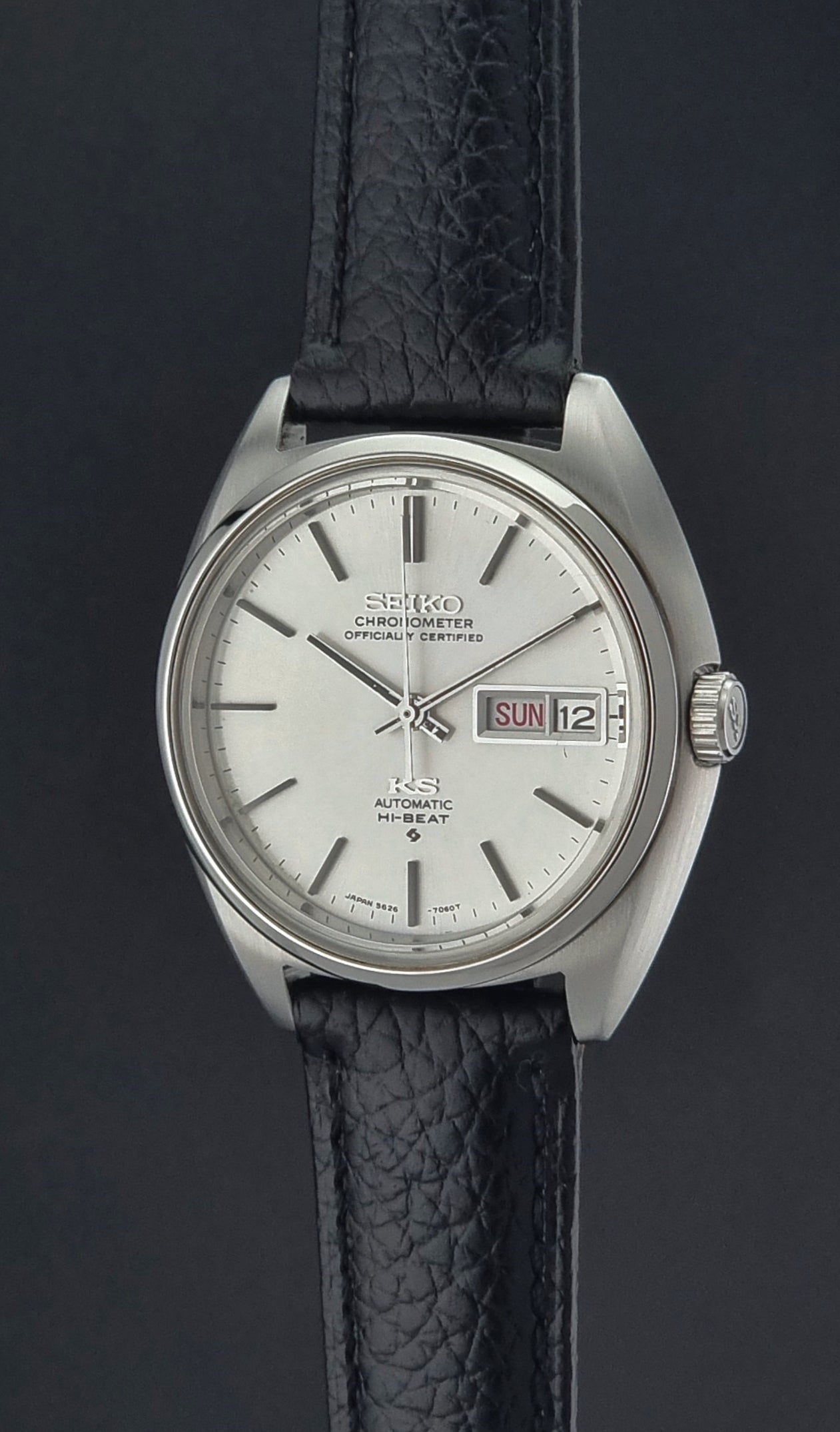 Vintage King Seiko 5626-7060 wristwatch with a silver case and black leather strap on a dark surface crown profile