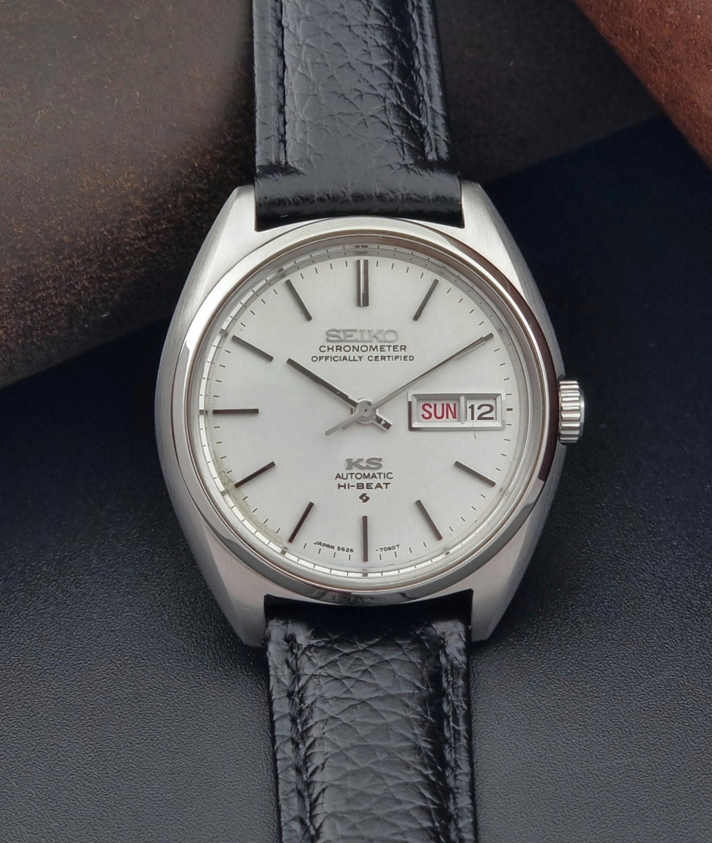 Vintage King Seiko 5626-7060 wristwatch with a silver case and black leather strap on a dark surface close up dial 