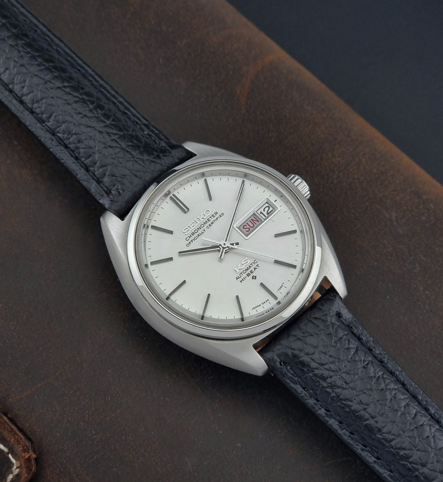 Vintage King Seiko 5626-7060 wristwatch with a silver case and black leather strap on a dark surface