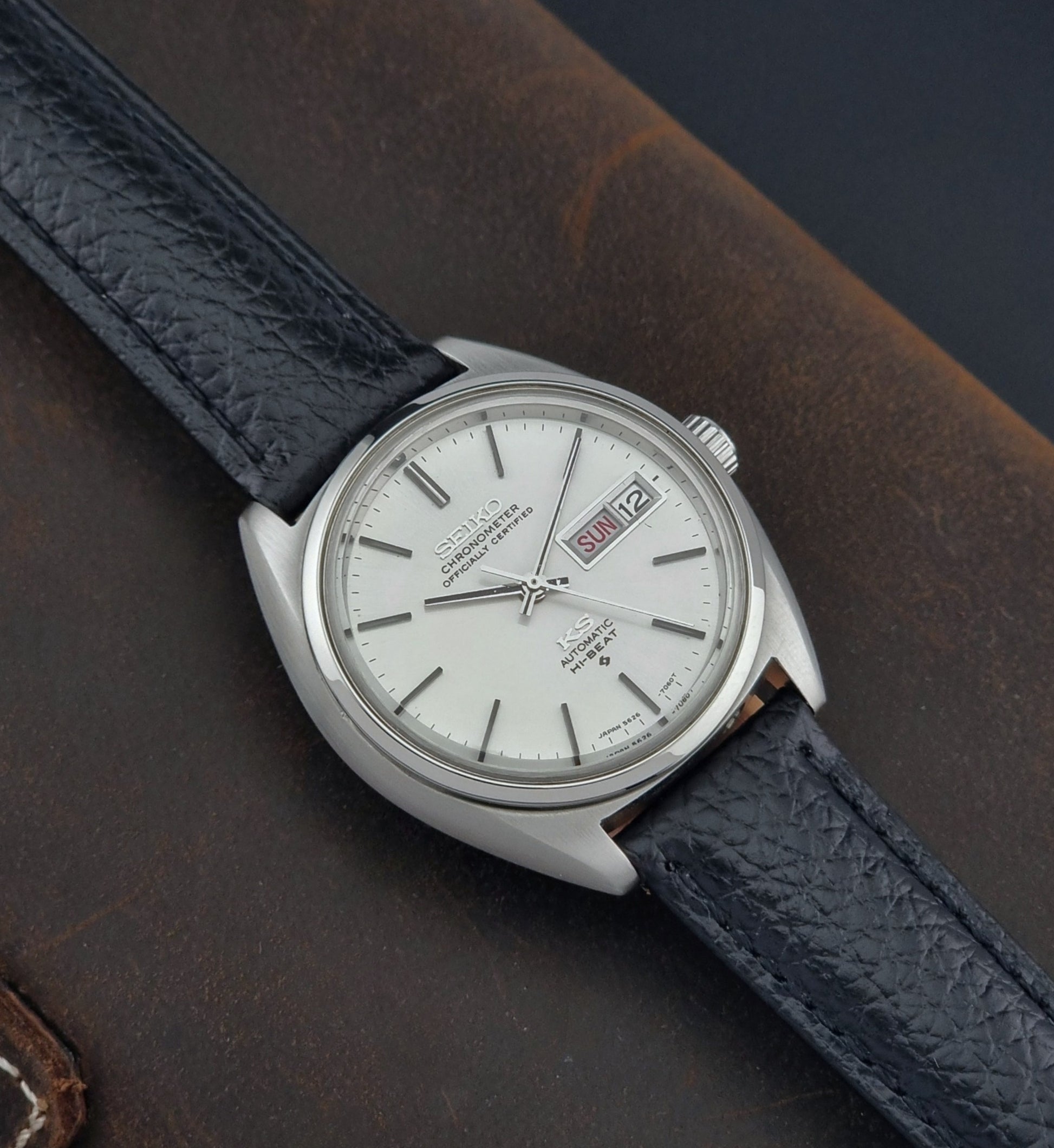 Vintage King Seiko 5626-7060 wristwatch with a silver case and black leather strap on a dark surface