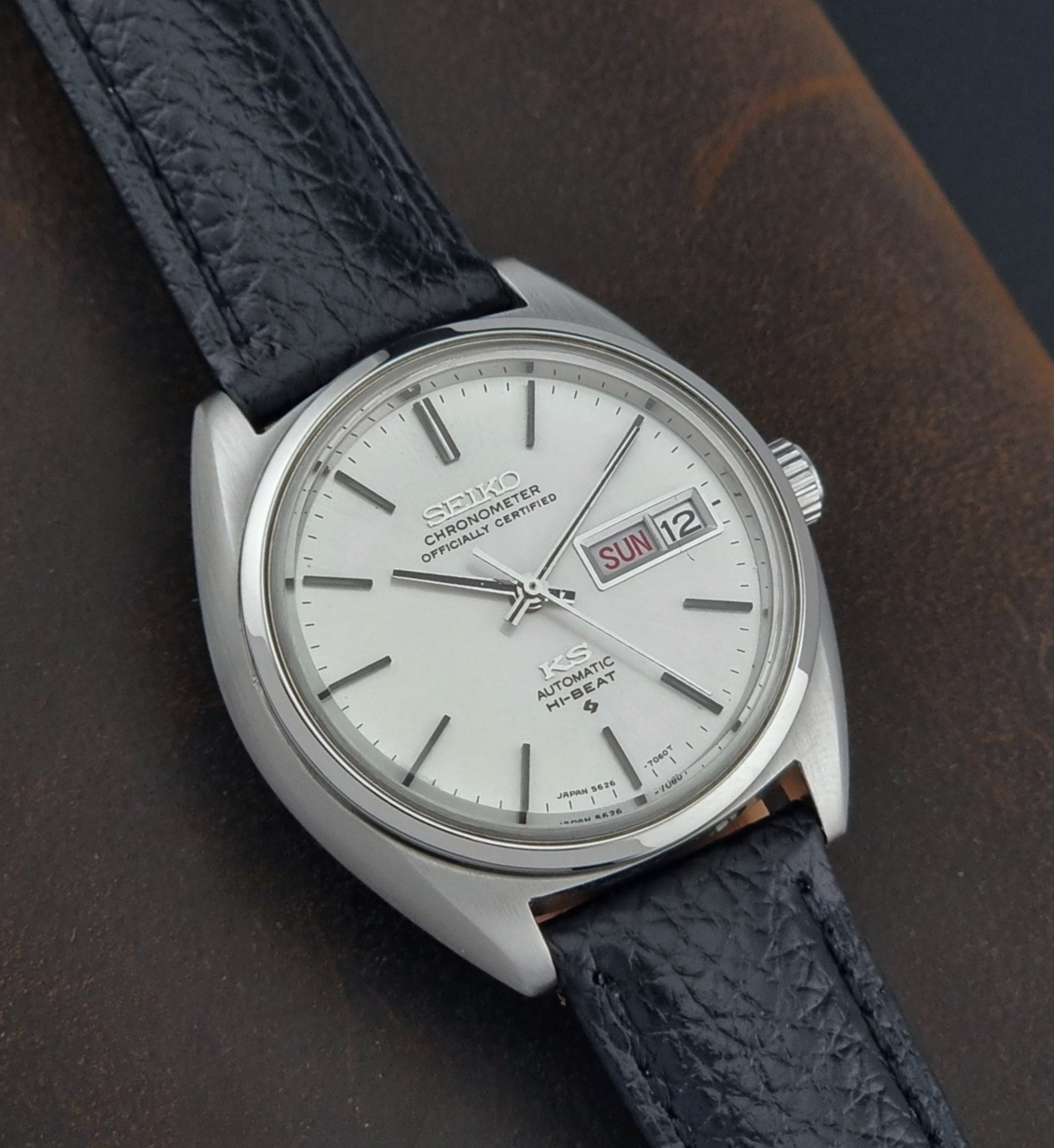 Vintage King Seiko 5626-7060 wristwatch with a silver case and black leather strap on a dark surface close up 