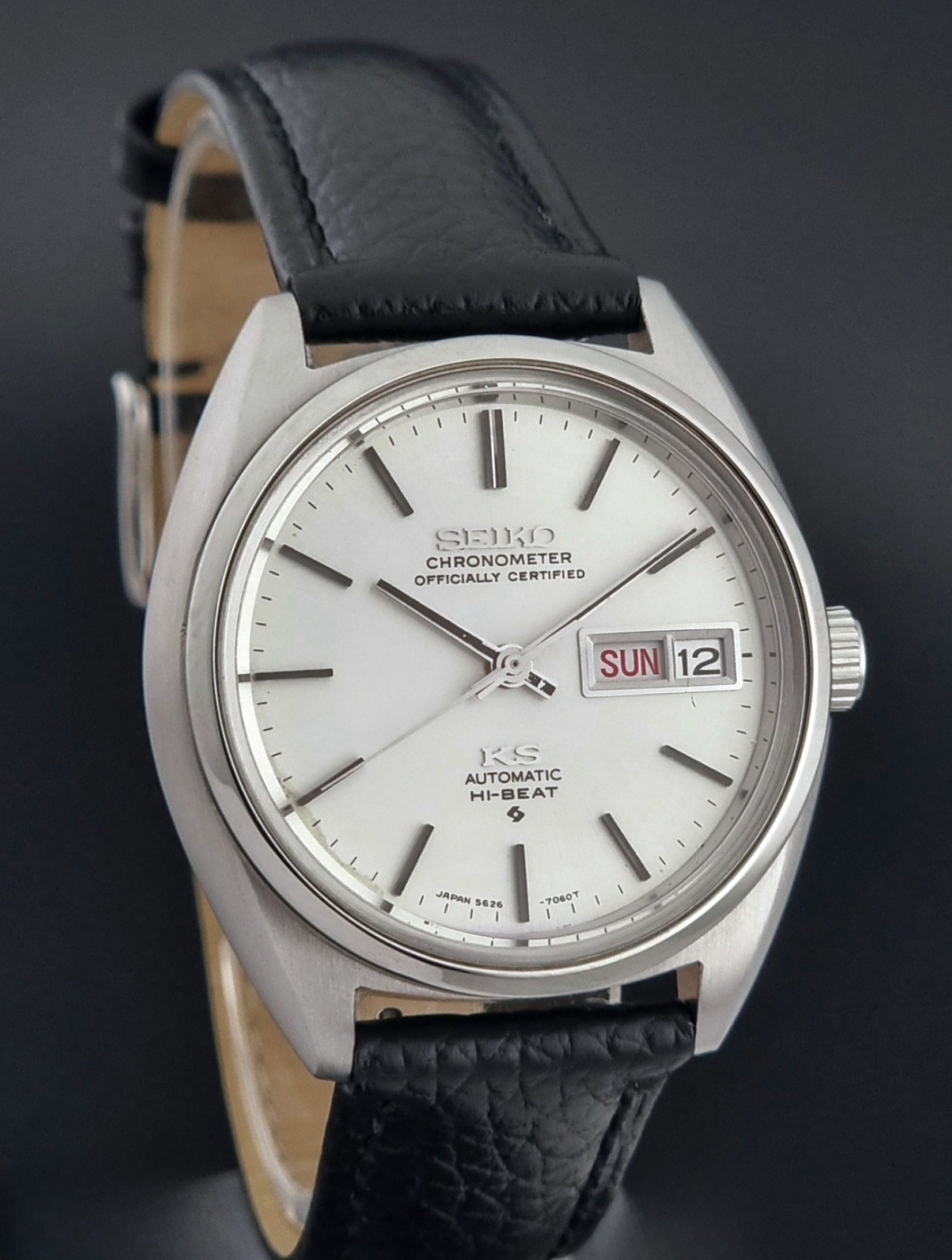 Vintage King Seiko 5626-7060 wristwatch with a silver case and black leather strap on a dark surface dial view