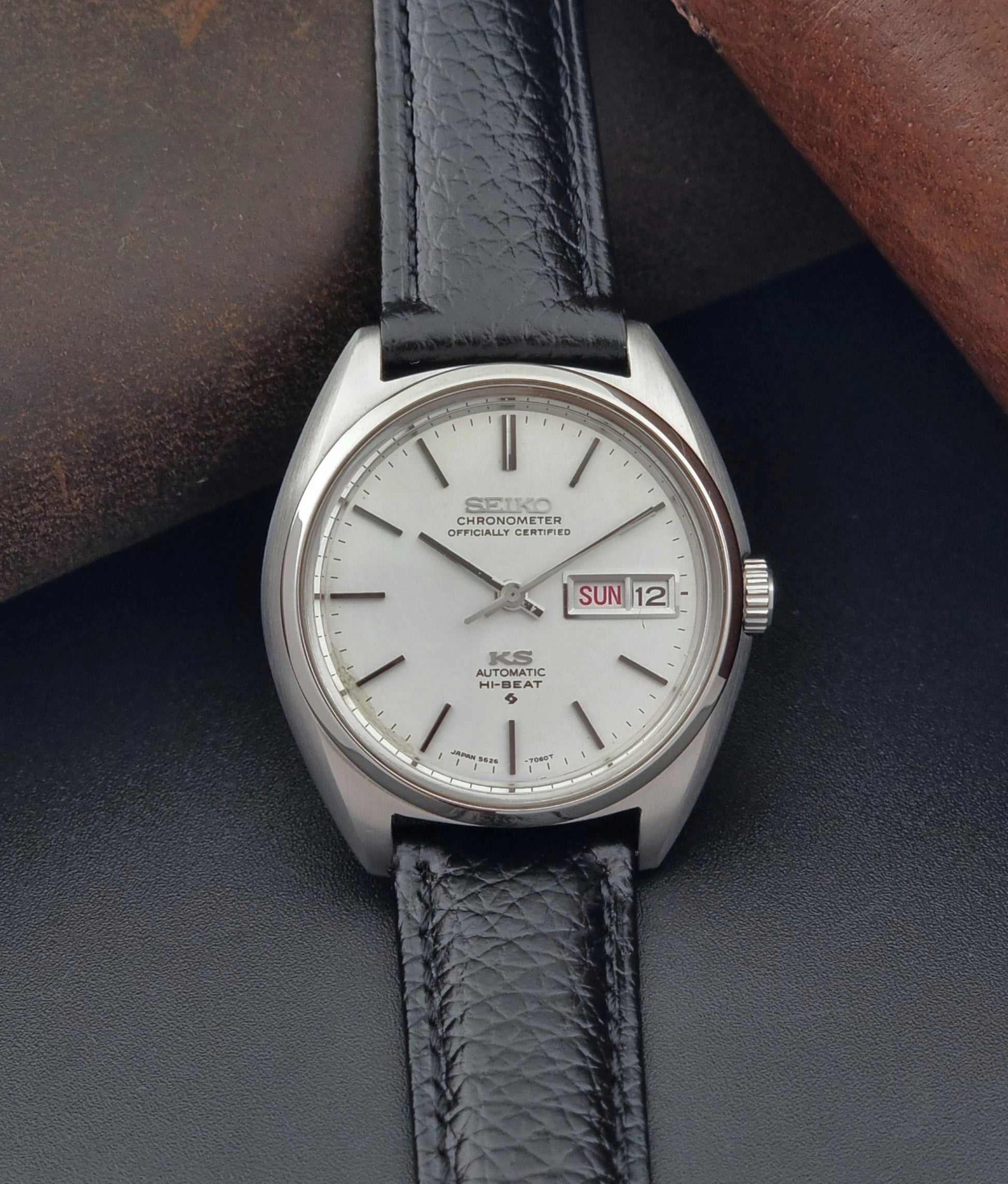 Vintage King Seiko 5626-7060 wristwatch with a silver case and black leather strap on a dark surface front view