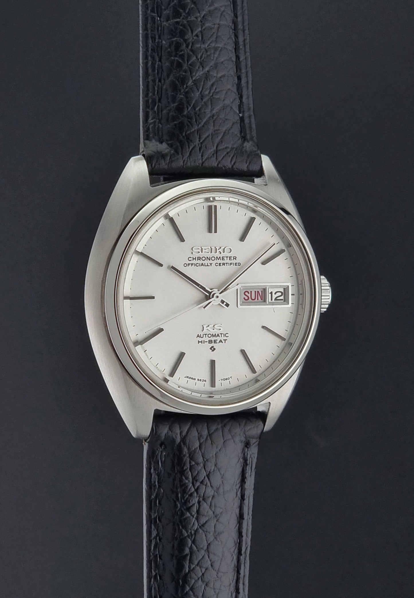 Vintage King Seiko 5626-7060 wristwatch with a silver case and black leather strap on a dark surface side profile