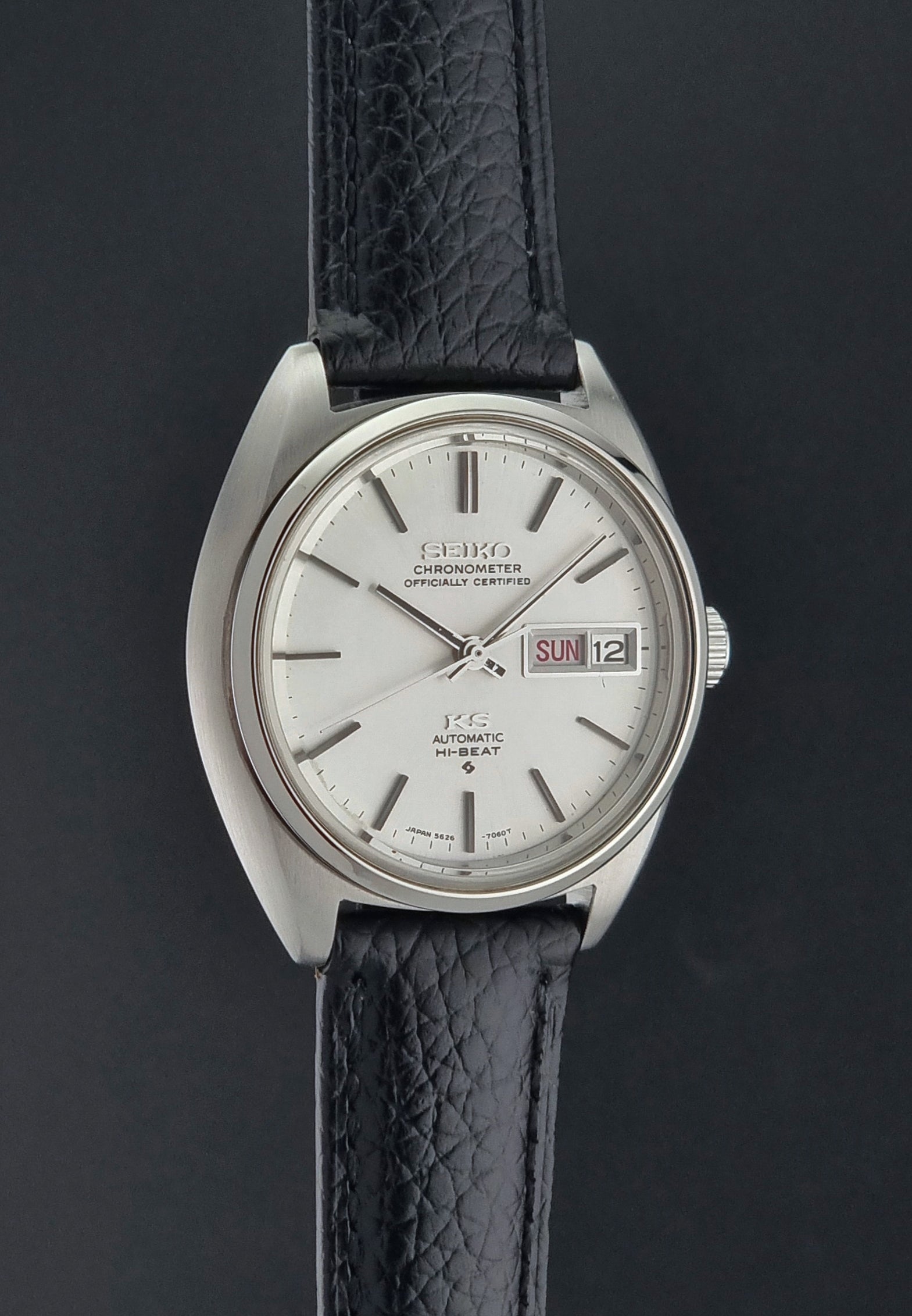 Vintage King Seiko 5626-7060 wristwatch with a silver case and black leather strap on a dark surface side profile