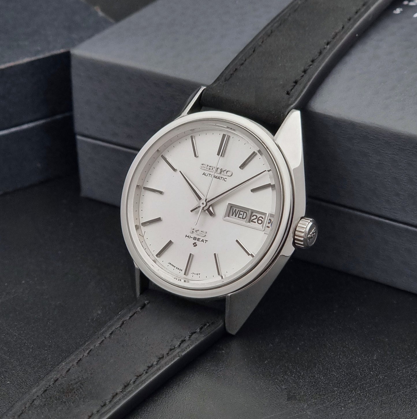 Vintage King Seiko 5626-7110 wristwatch with black leather strap on a gray background crown view