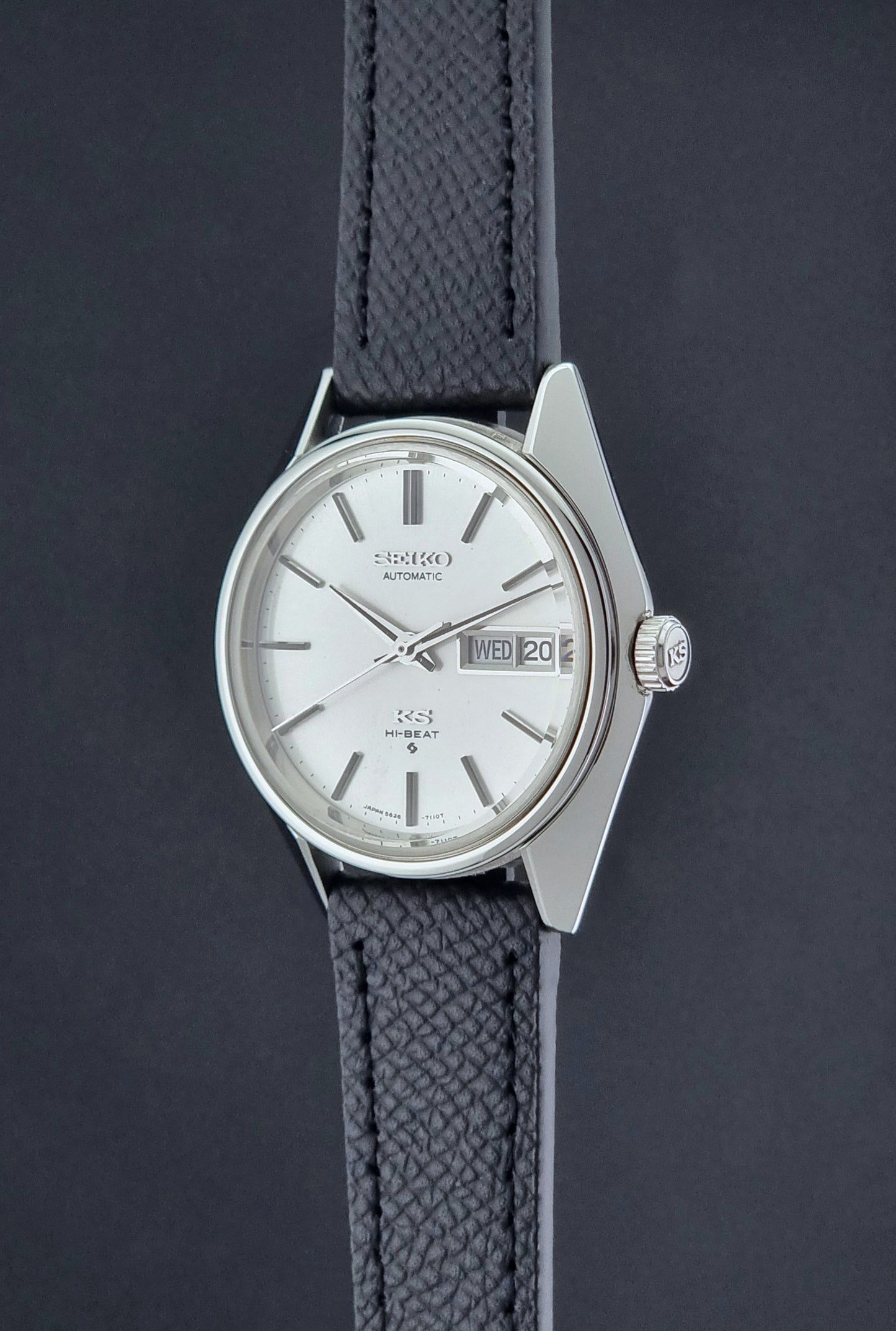 Vintage King Seiko 5626-7110 Wristwatch with a silver case and black strap on a dark gray background crown profile view