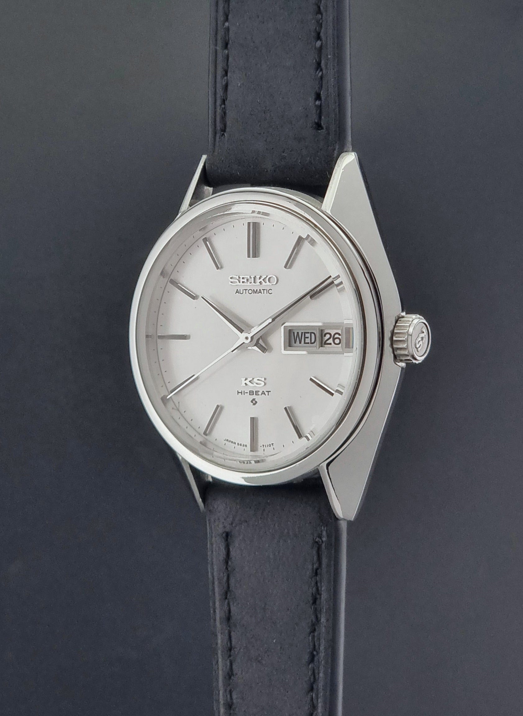 Vintage King Seiko 5626-7110 wristwatch with black leather strap on a gray background crown profile view