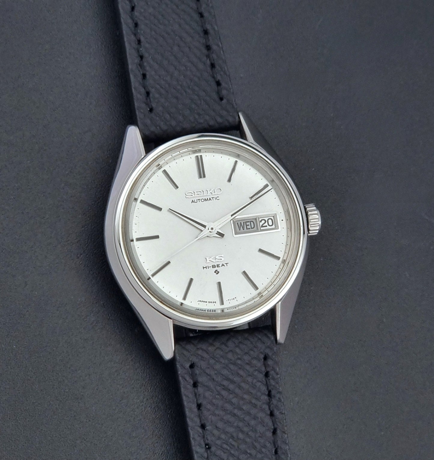 Vintage King Seiko 5626-7110 Wristwatch with a silver case and black strap on a dark gray background front view