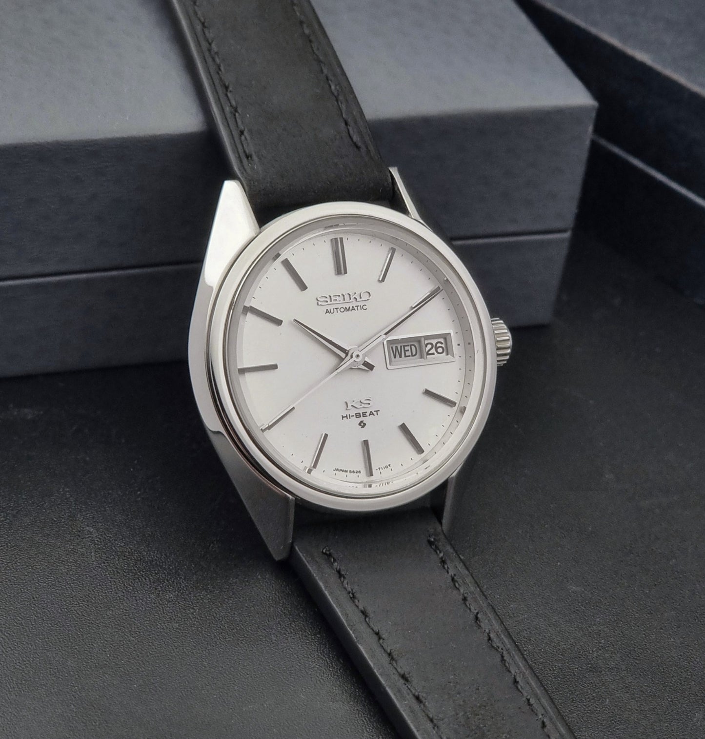 Vintage King Seiko 5626-7110 wristwatch with black leather strap on a gray background side view