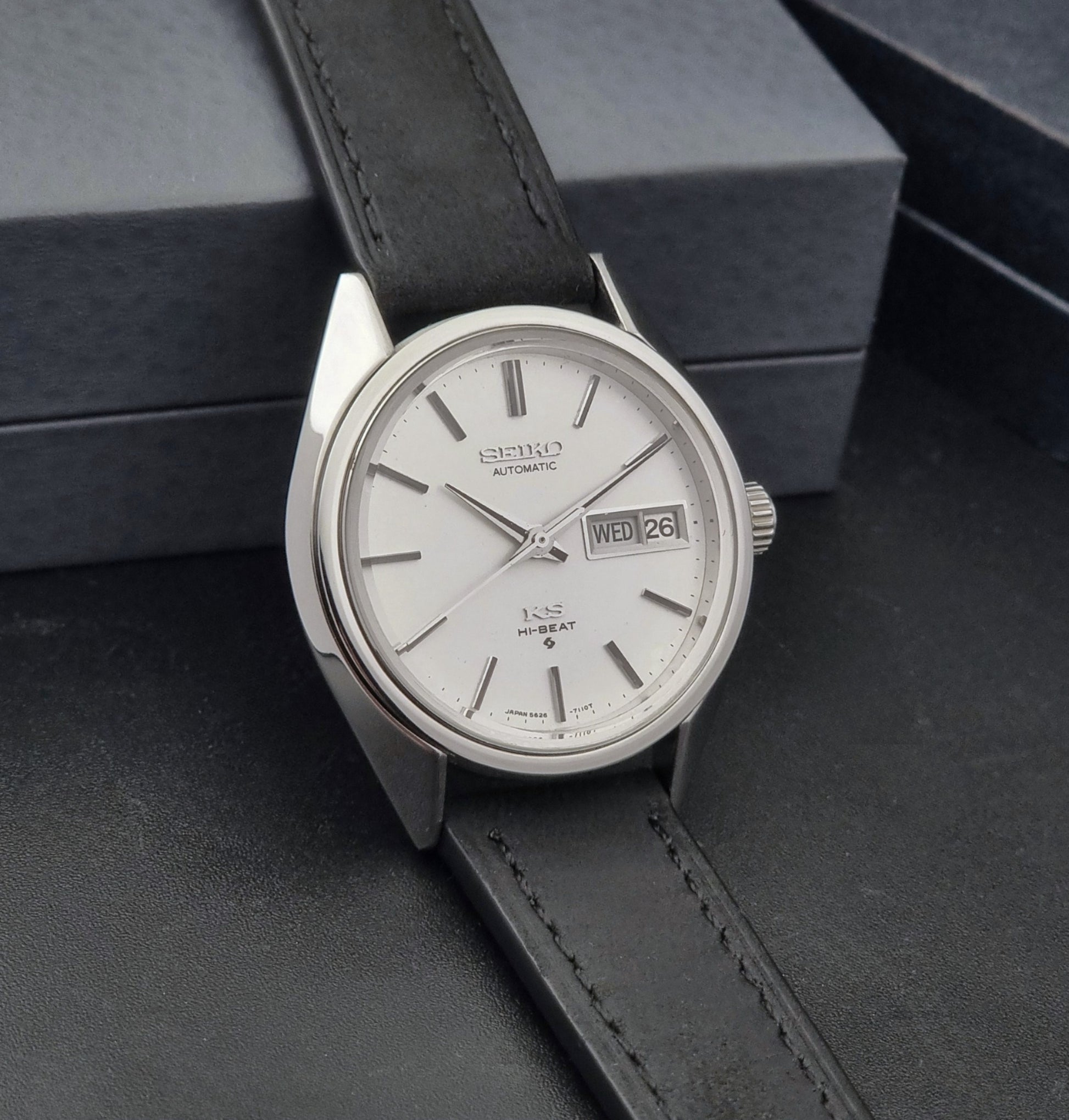 Vintage King Seiko 5626-7110 wristwatch with black leather strap on a gray background side view
