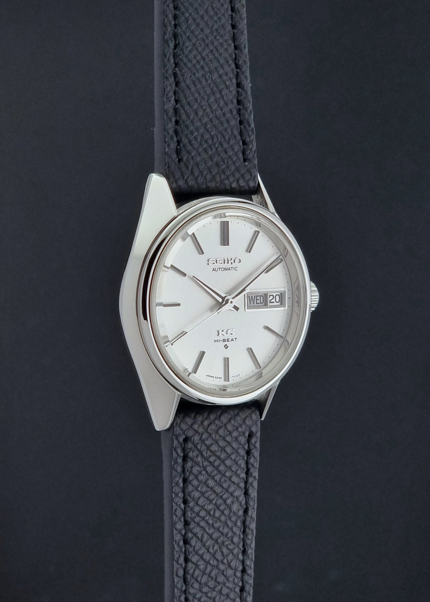 Vintage King Seiko 5626-7110 Wristwatch with a silver case and black strap on a dark gray background side profile view