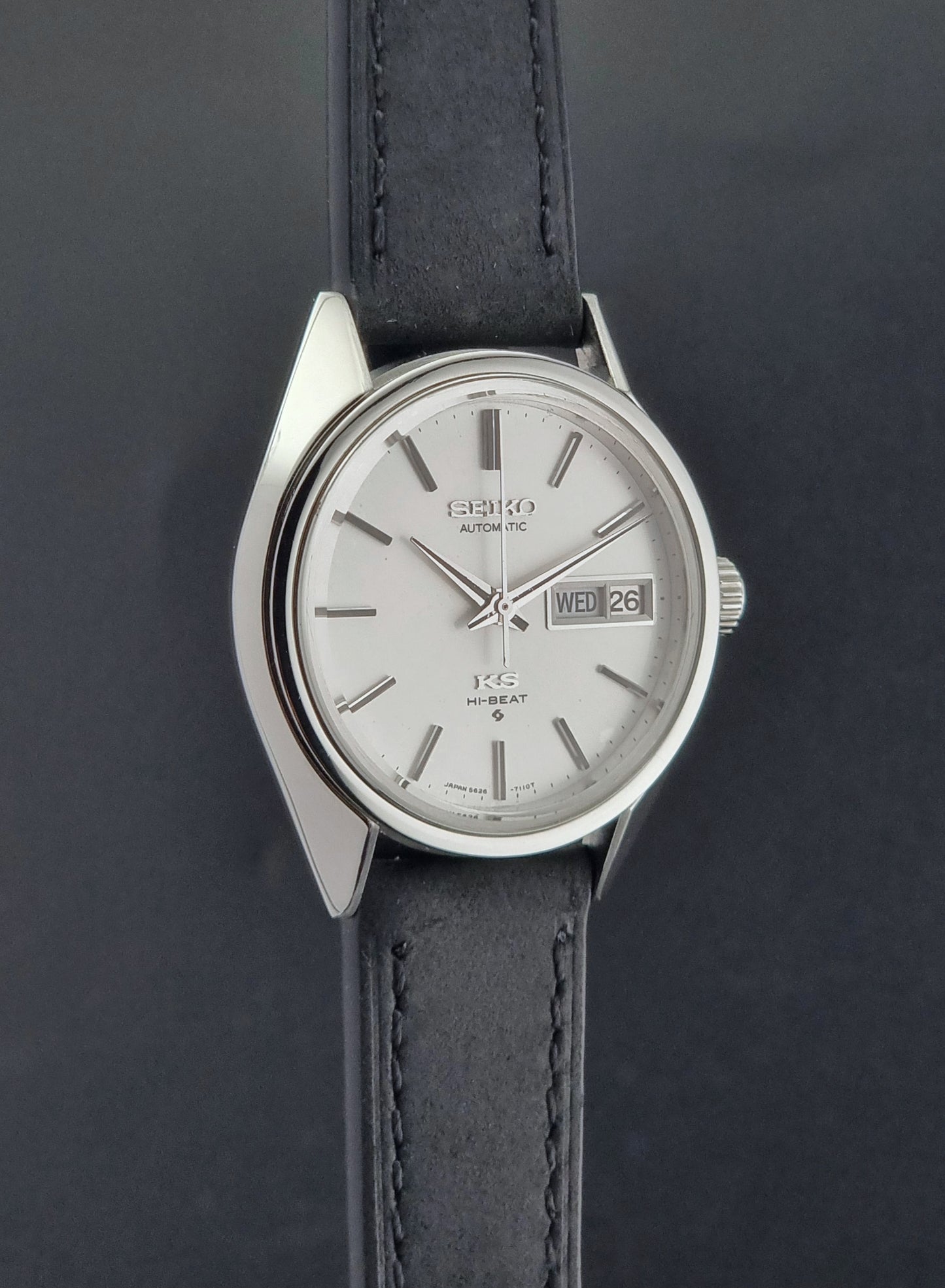 Vintage King Seiko 5626-7110 wristwatch with black leather strap on a gray background side profile view