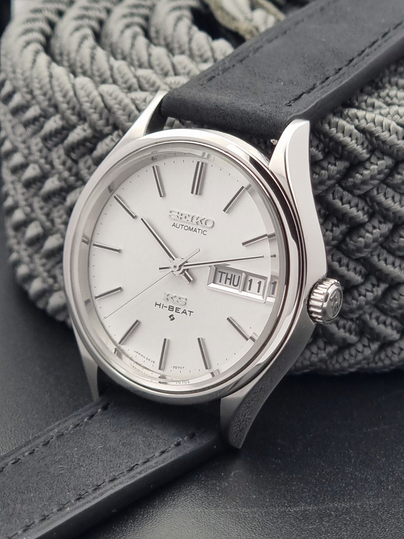 Vintage King Seiko Wristwatch Hi-beat 5626-7120 with a black strap on a textured gray background crown side view