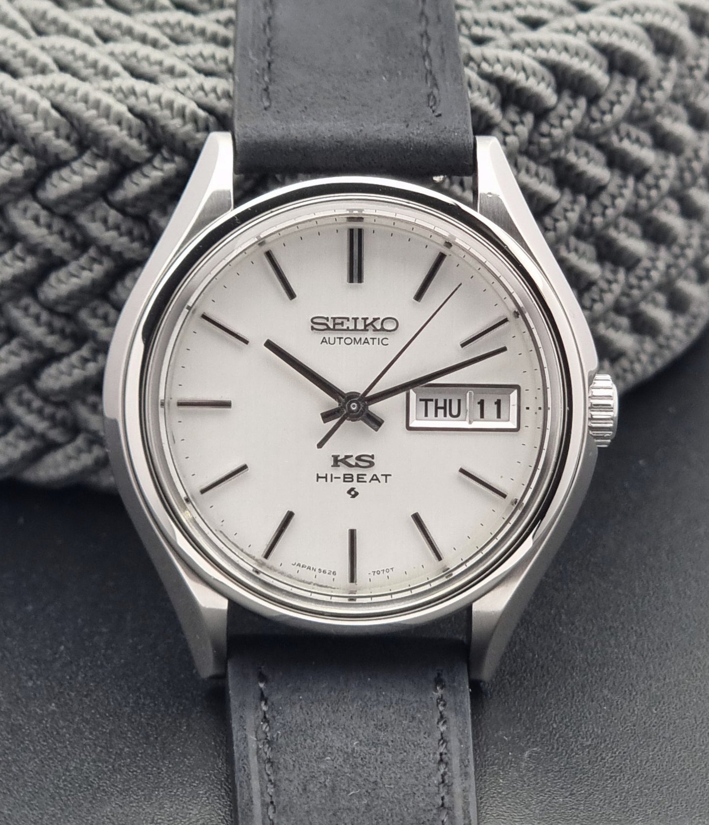 Vintage King Seiko Wristwatch Hi-beat 5626-7120 with a black strap on a textured gray background close up