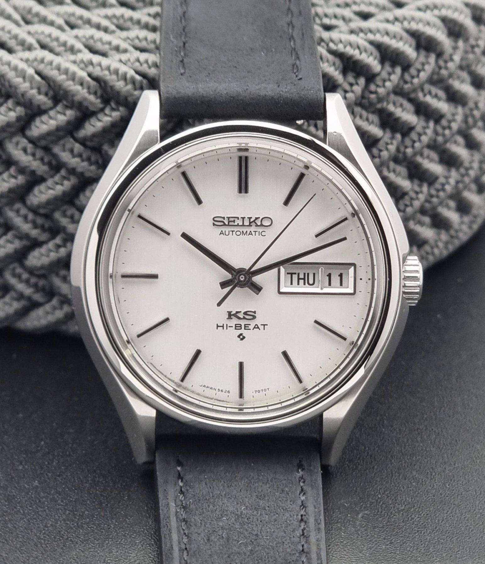 Vintage King Seiko Wristwatch Hi-beat 5626-7120 with a black strap on a textured gray background close up
