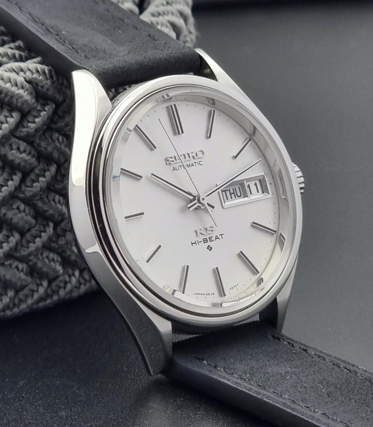 Vintage King Seiko Wristwatch Hi-beat 5626-7120 with a black strap on a textured gray background side view