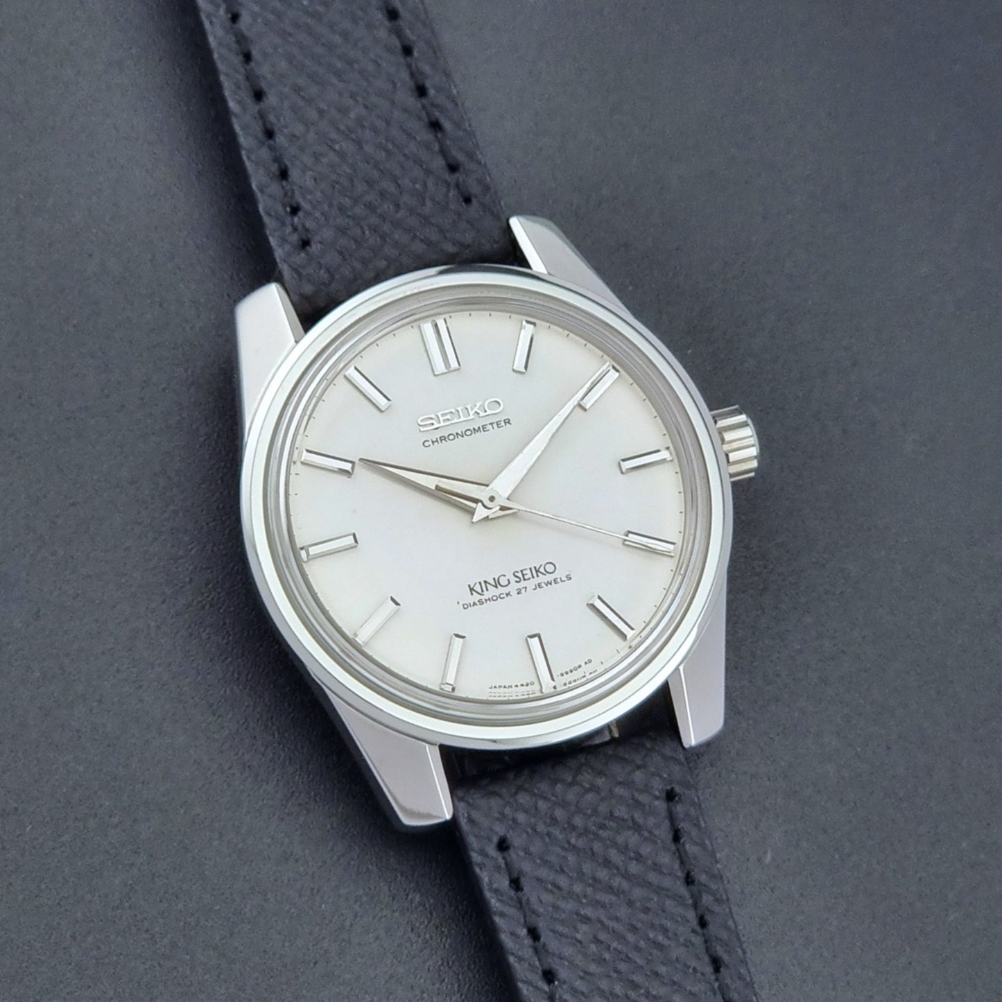 Vintage King Seiko Wristwatch 4420-9990 Chronometer with a black strap on a textured background front view