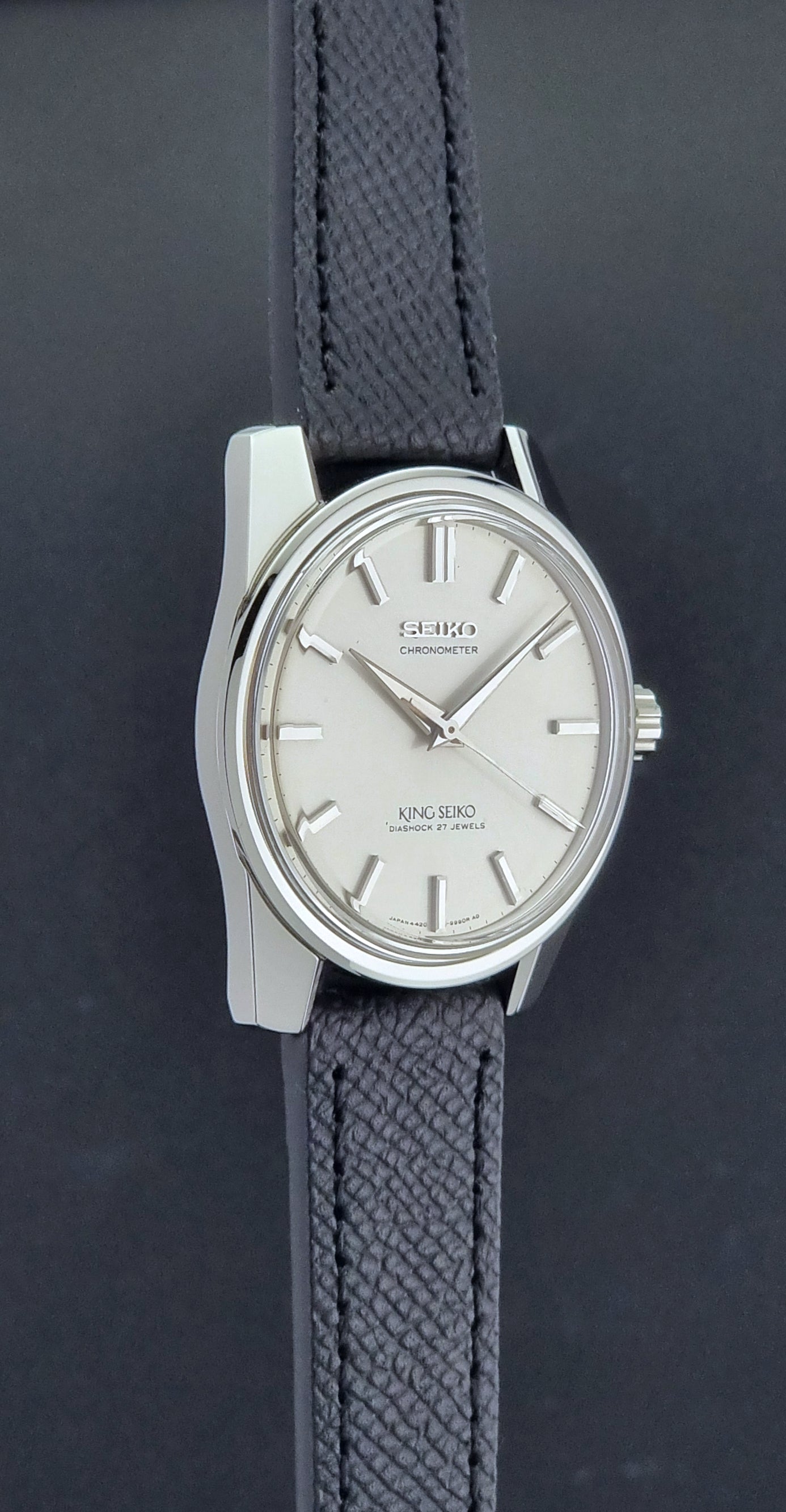Vintage King Seiko Wristwatch 4420-9990 Chronometer with a black strap on a textured background side profile view