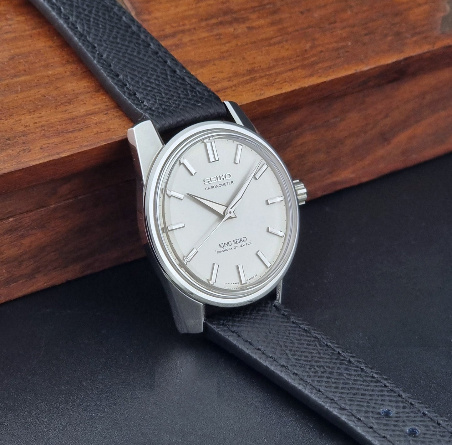 Vintage King Seiko Wristwatch 4420-9990 Chronometer with a black strap on a textured background side view