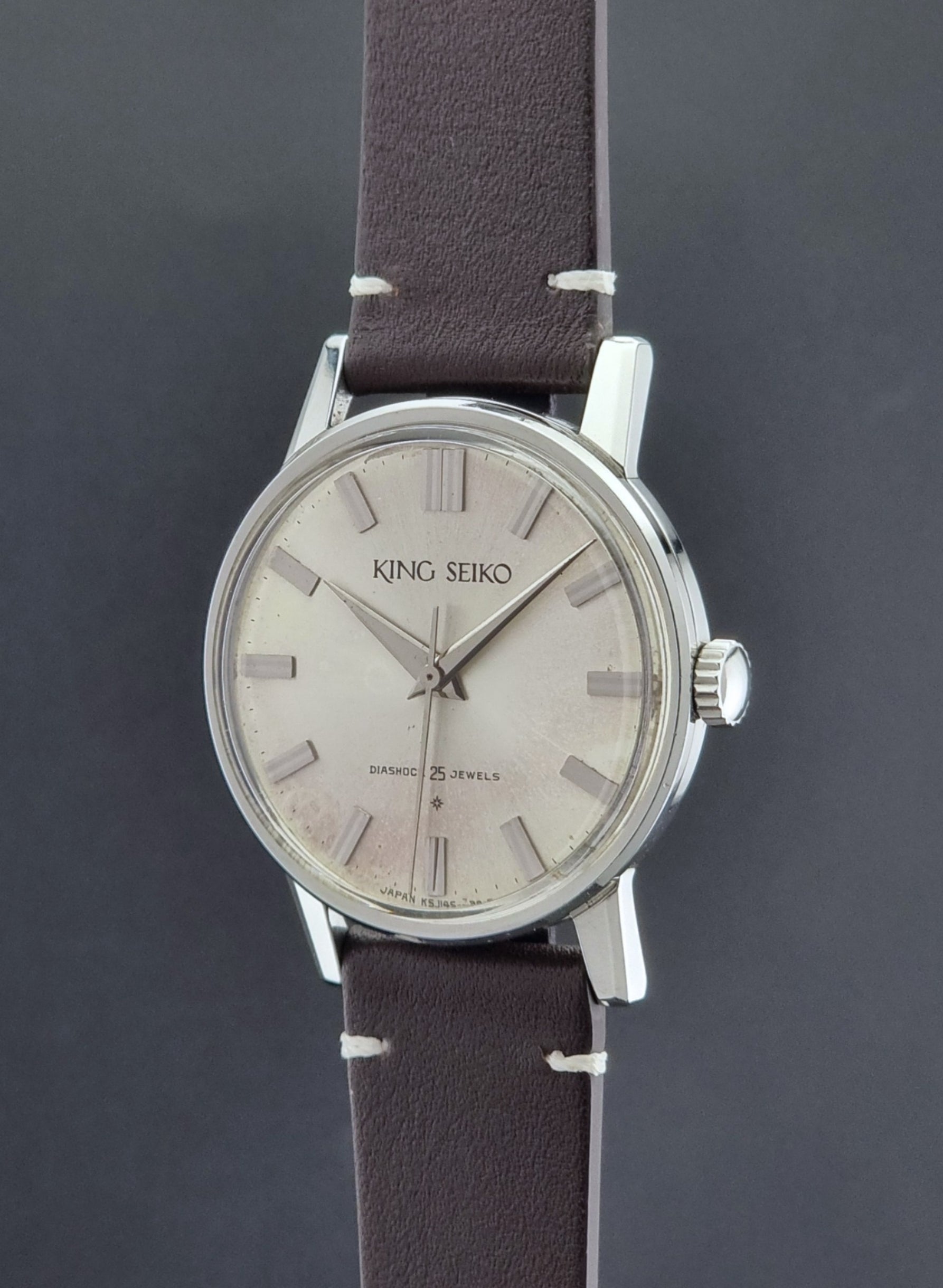 Vintage King Seiko J14102E Wristwatch with brown leather strap on a dark gray background crown profile