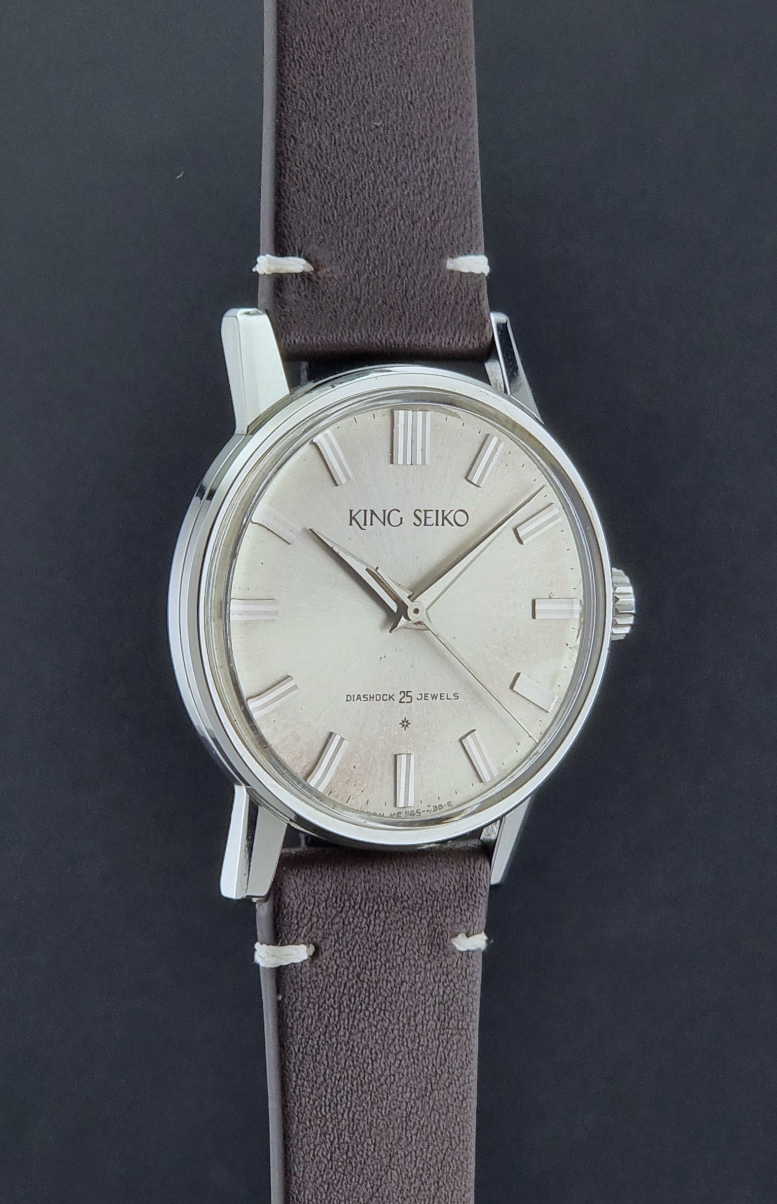 Vintage King Seiko J14102E Wristwatch with brown leather strap on a dark gray background side profile